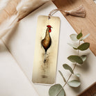Bookmark with a rooster design on a wooden surface with leaves and feathers.