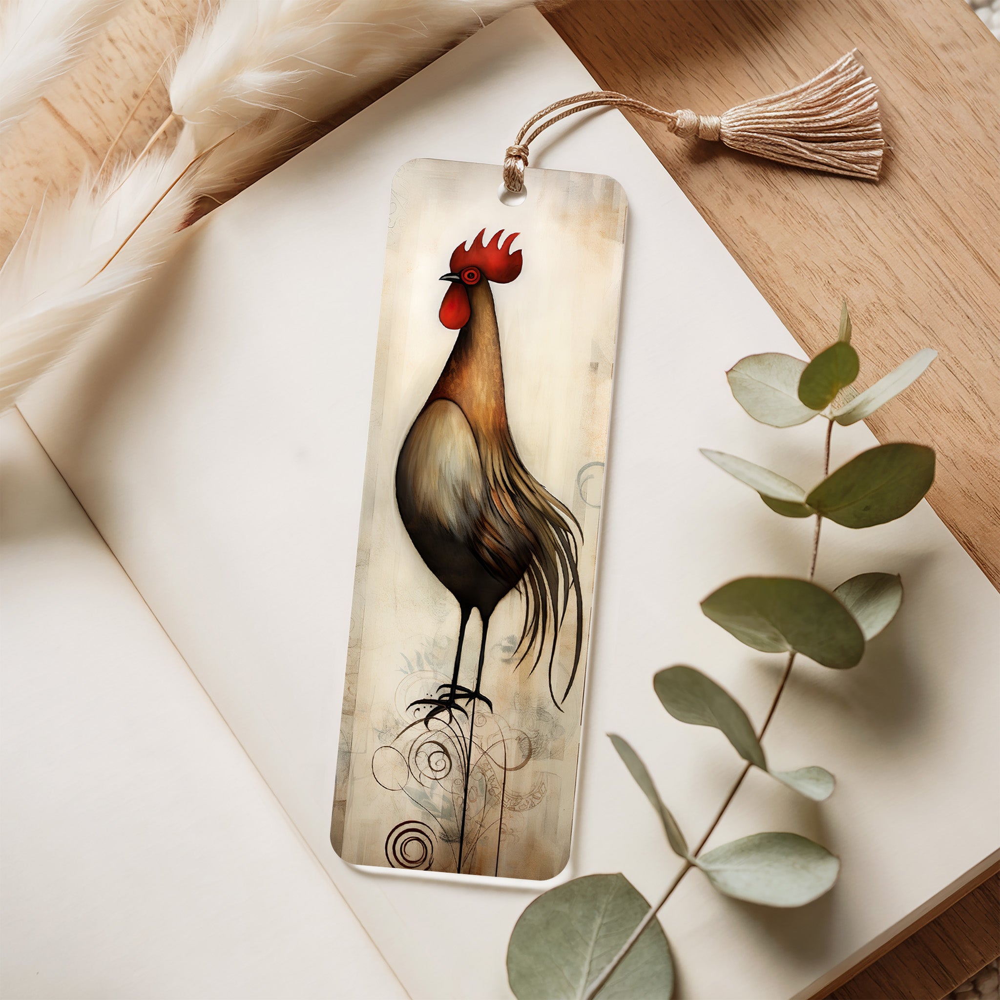 Decorative bookmark with a cockerel design on a wooden surface with eucalyptus leaves.