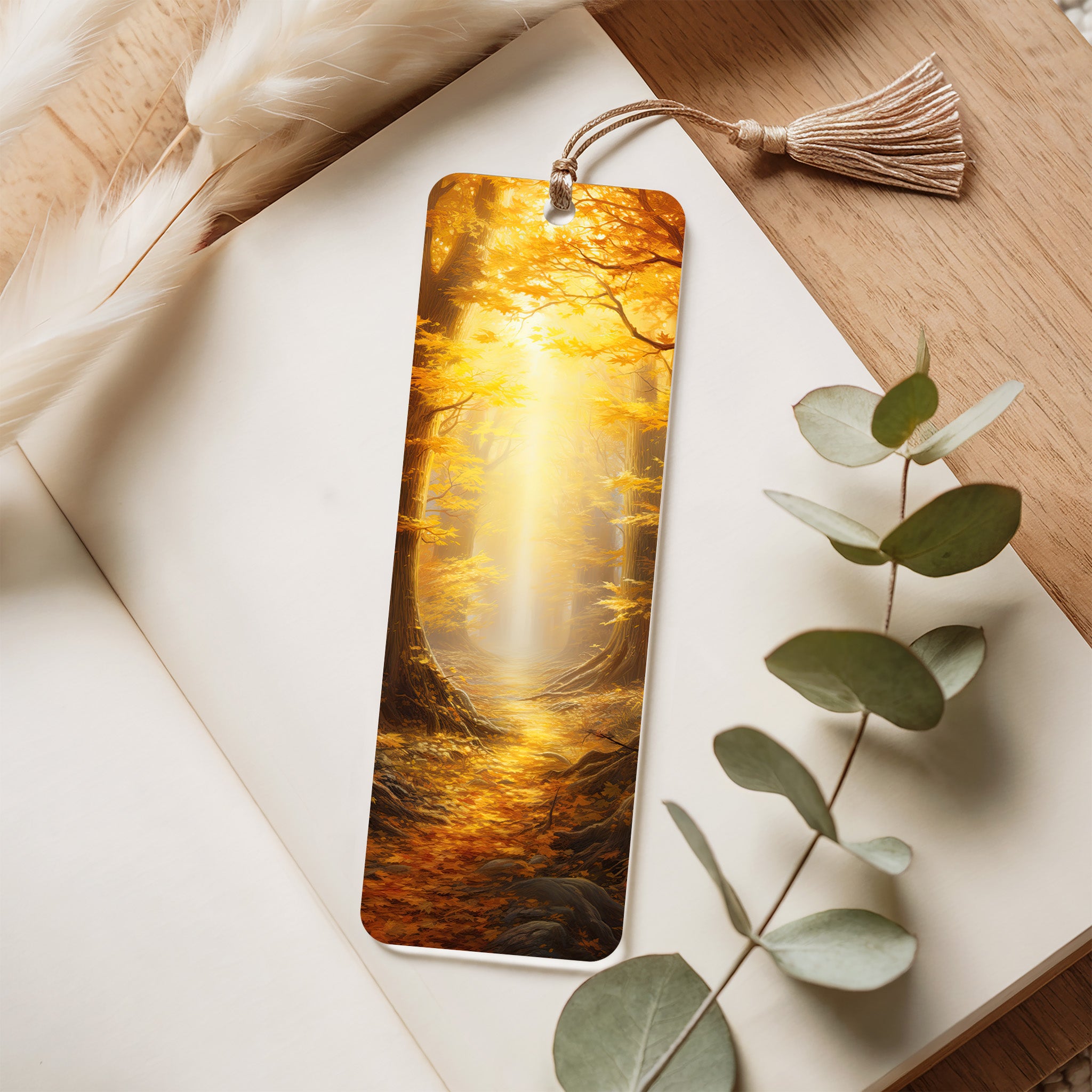 Bookmark with a scenic design of a forest and waterfall on a wooden surface with eucalyptus leaves.