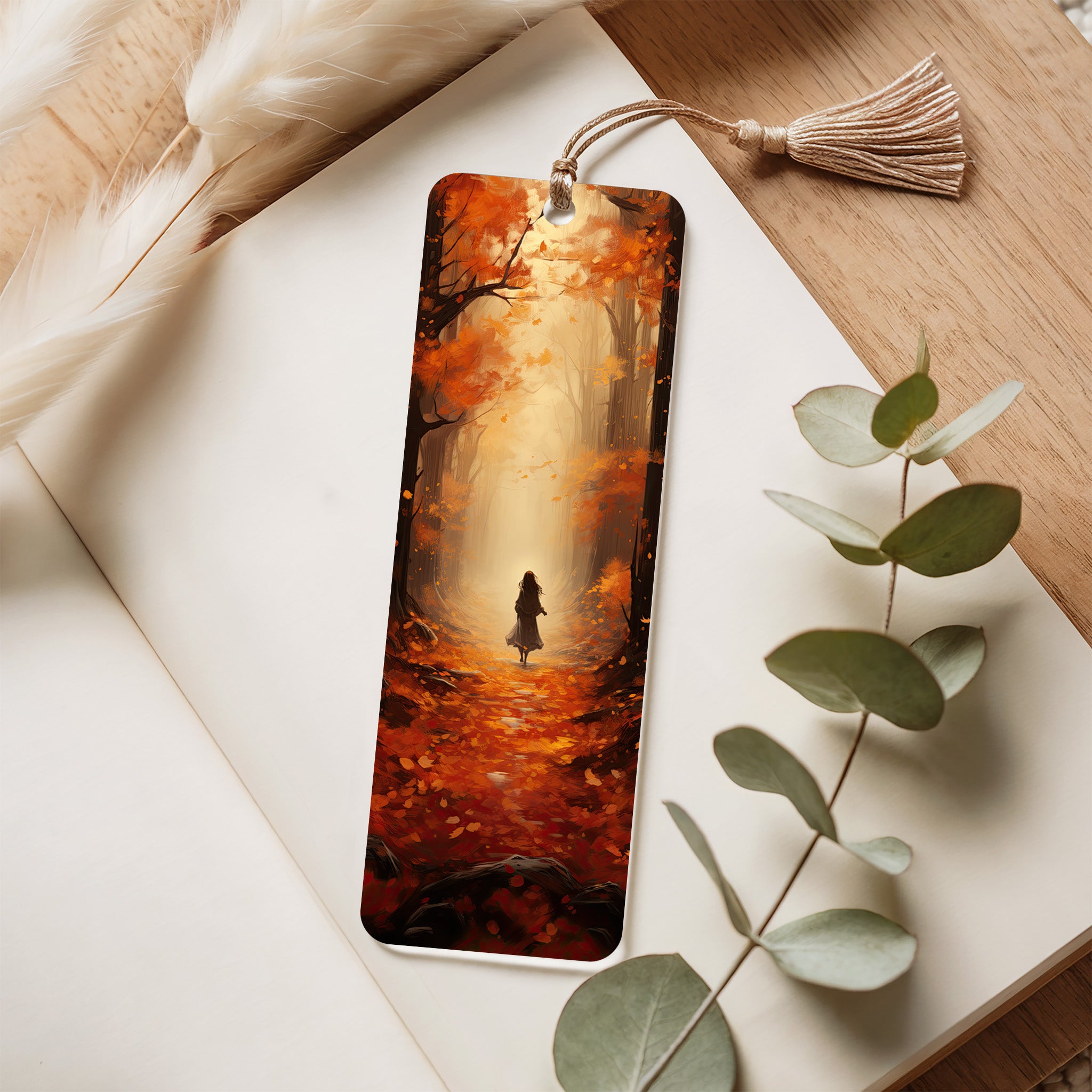 Decorative acrylic bookmark with a scenic design of a person walking through a forest, placed on a wooden surface with eucalyptus leaves.