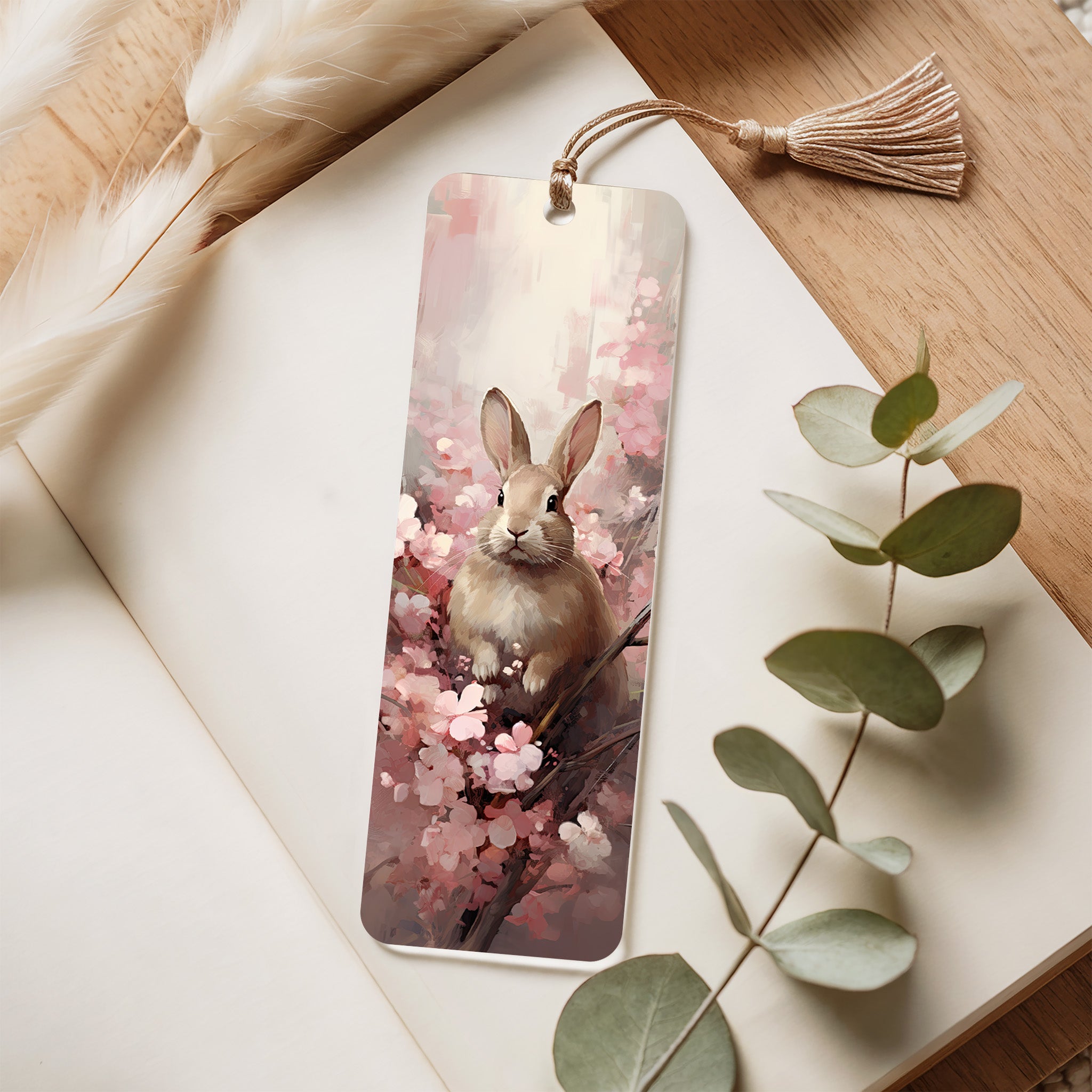 Bookmark with a rabbit and cherry blossoms design on a wooden surface with eucalyptus leaves.