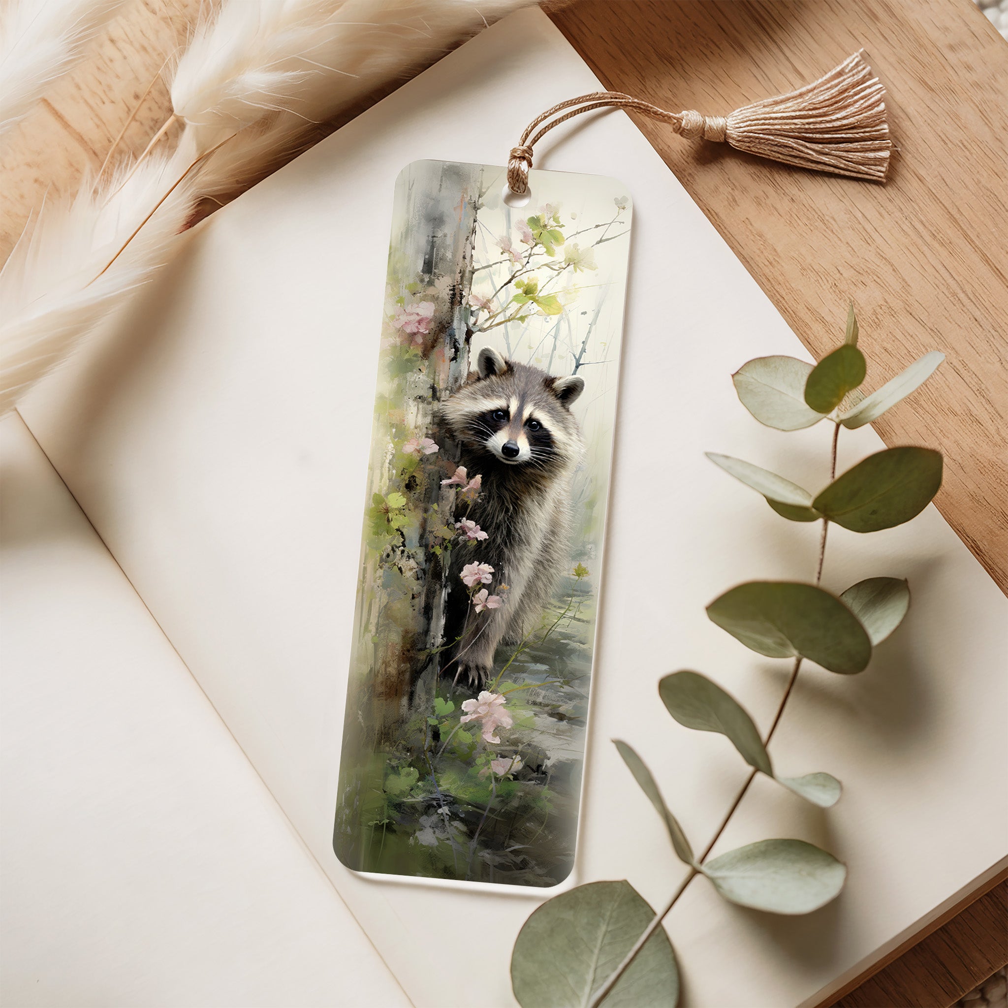 Bookmark with raccoon illustration on a wooden surface with eucalyptus leaves