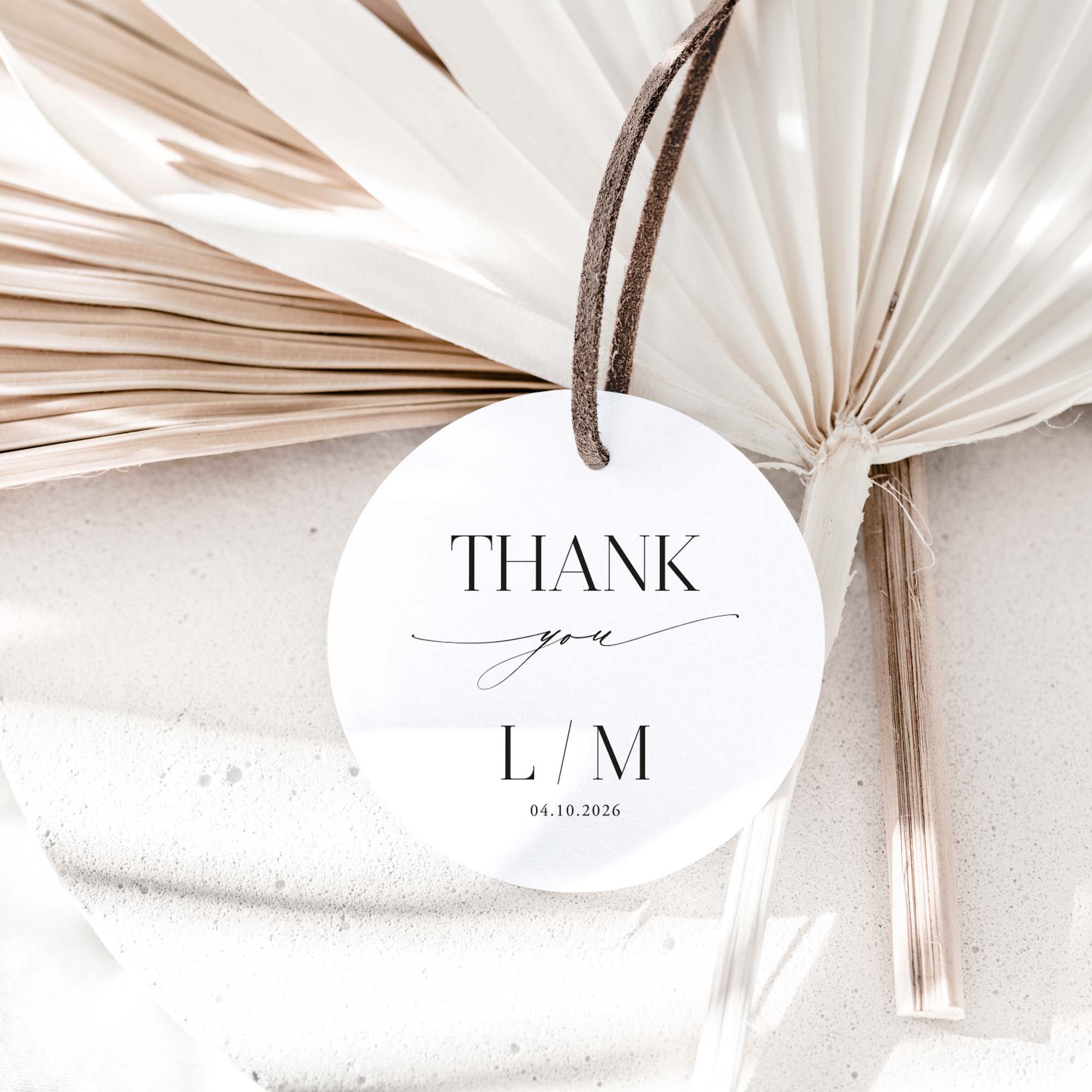 Round white card with 'Thank you L/M' text, tied with a string against a textured beige background.