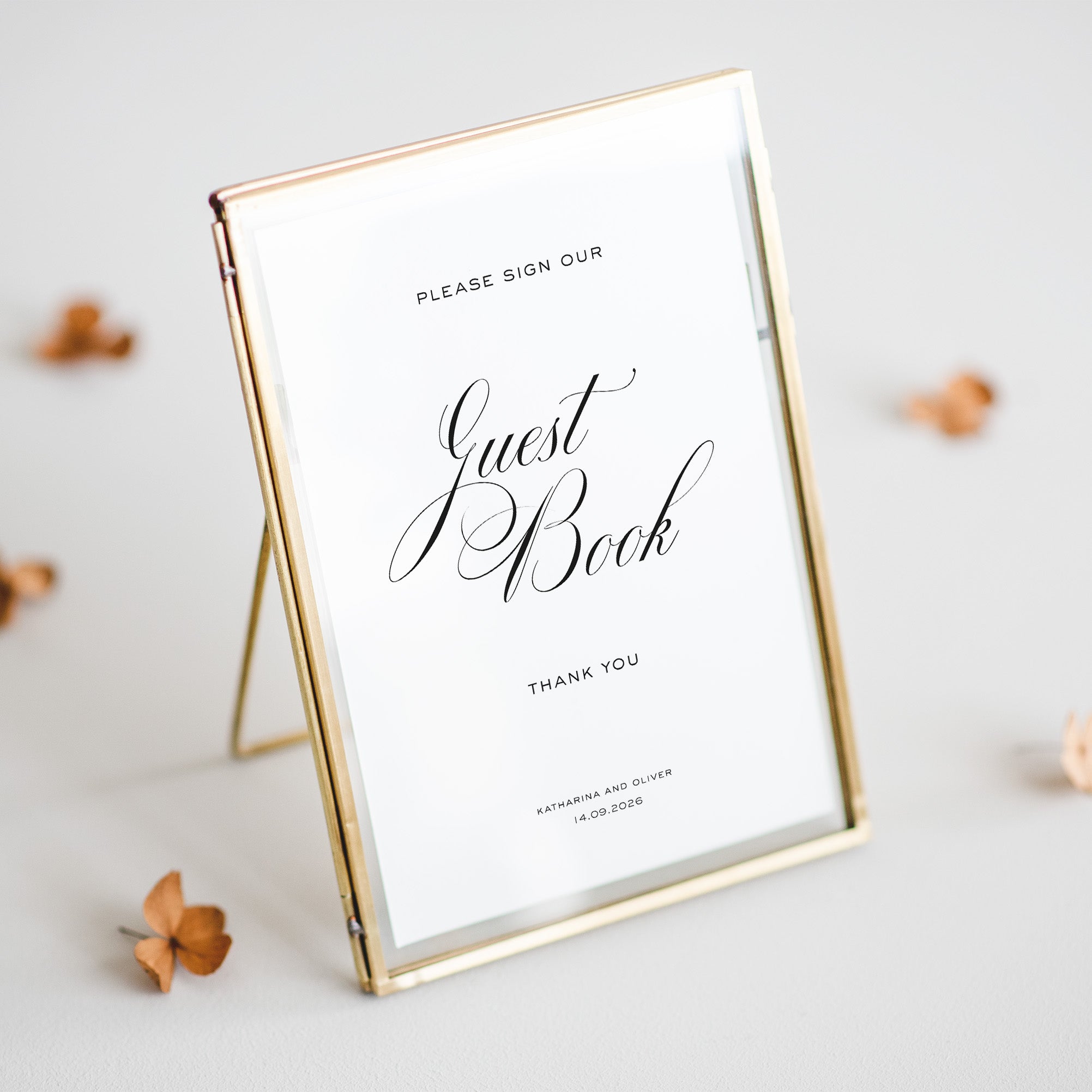 Gold-framed sign inviting guests to sign a guest book with personalized text.