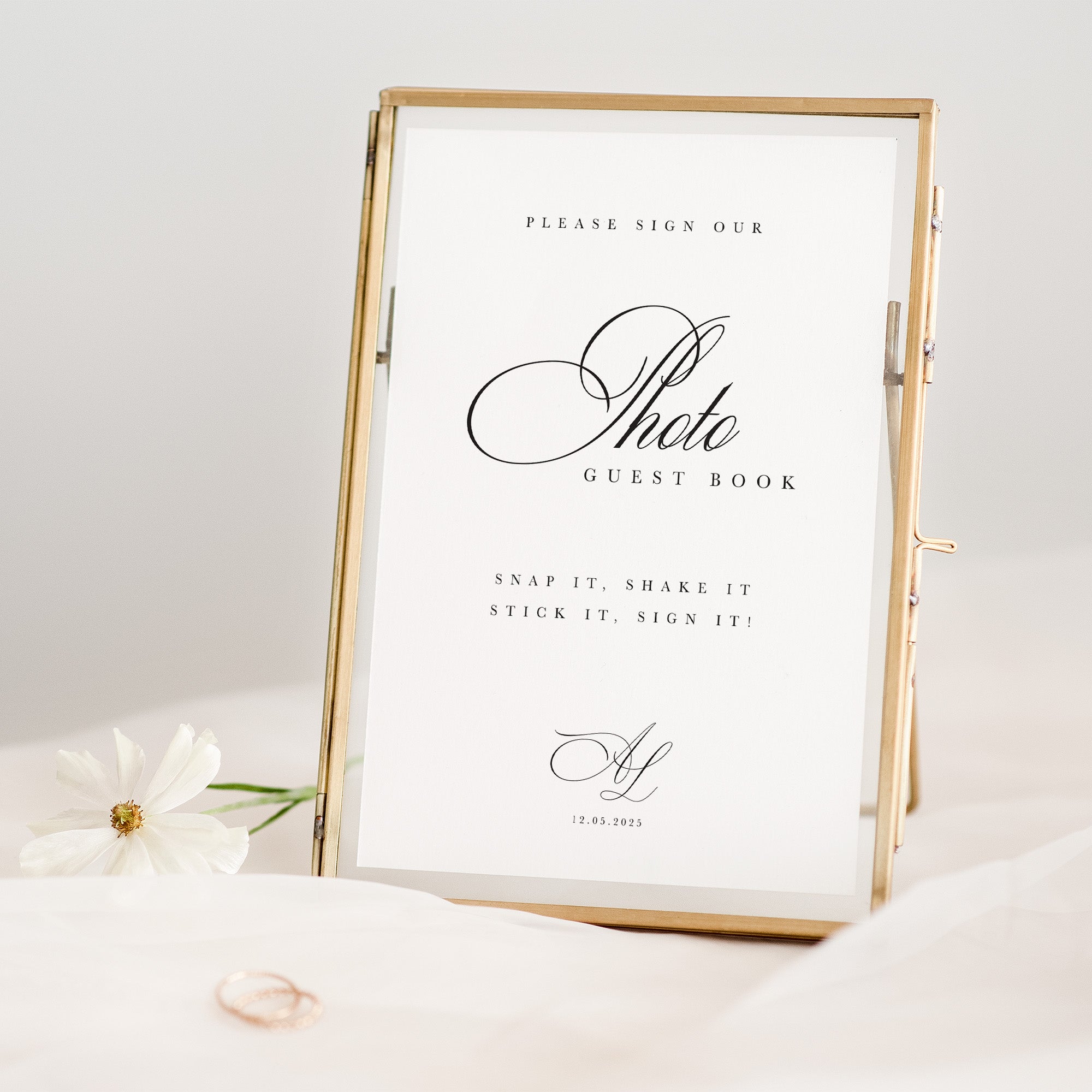Gold-framed photo guest book sign with white paper and decorative flowers on a light background