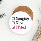Round white coaster with text 'Naughty, Nice, I Tried' on a white background