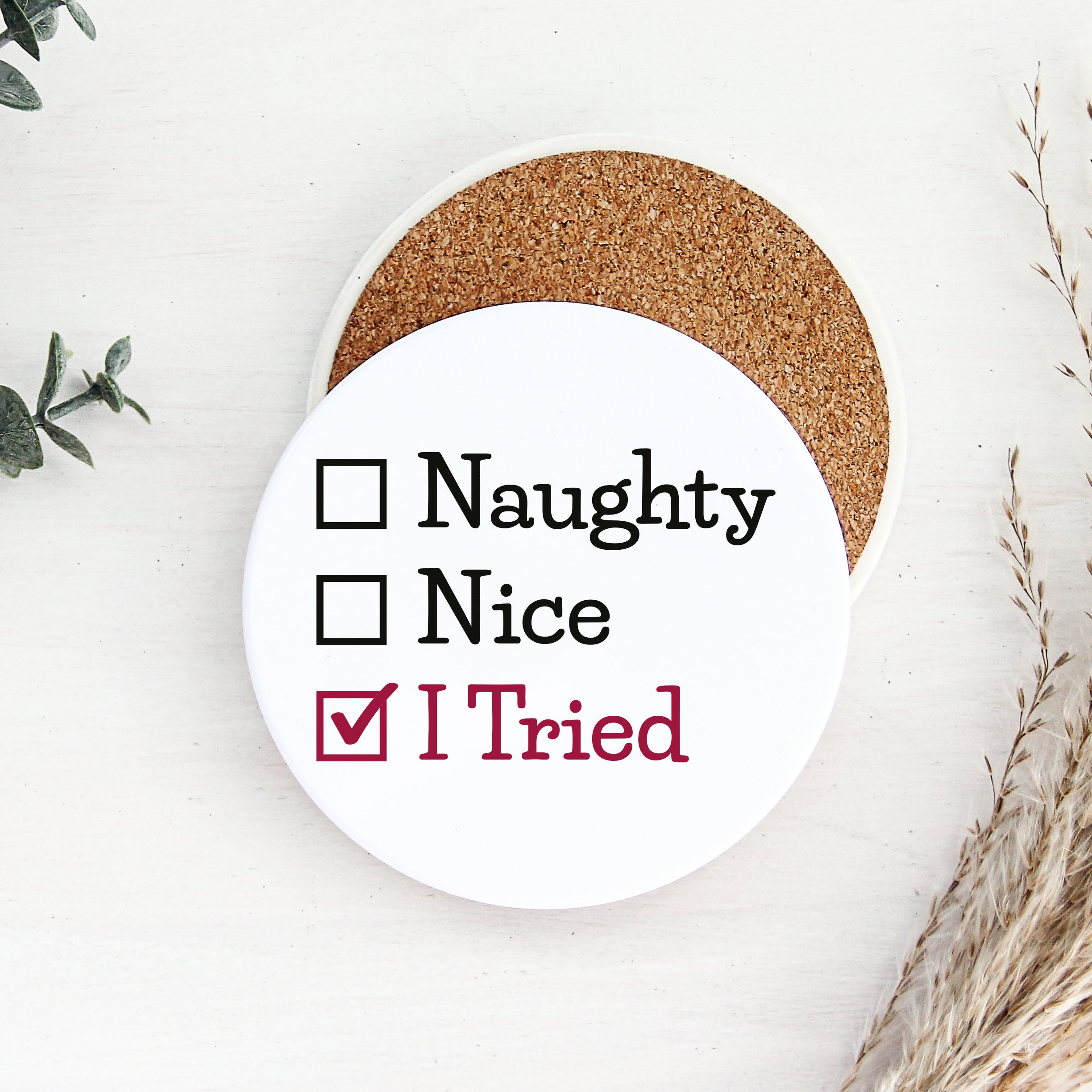 Round white coaster with text 'Naughty, Nice, I Tried' on a white background