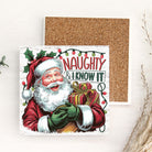 Christmas ceramic coaster with Santa Claus holding a gift and text 'Naughty & I know it' on a cork board background.