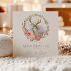 Christmas card with deer and floral wreath design on a blurred festive background