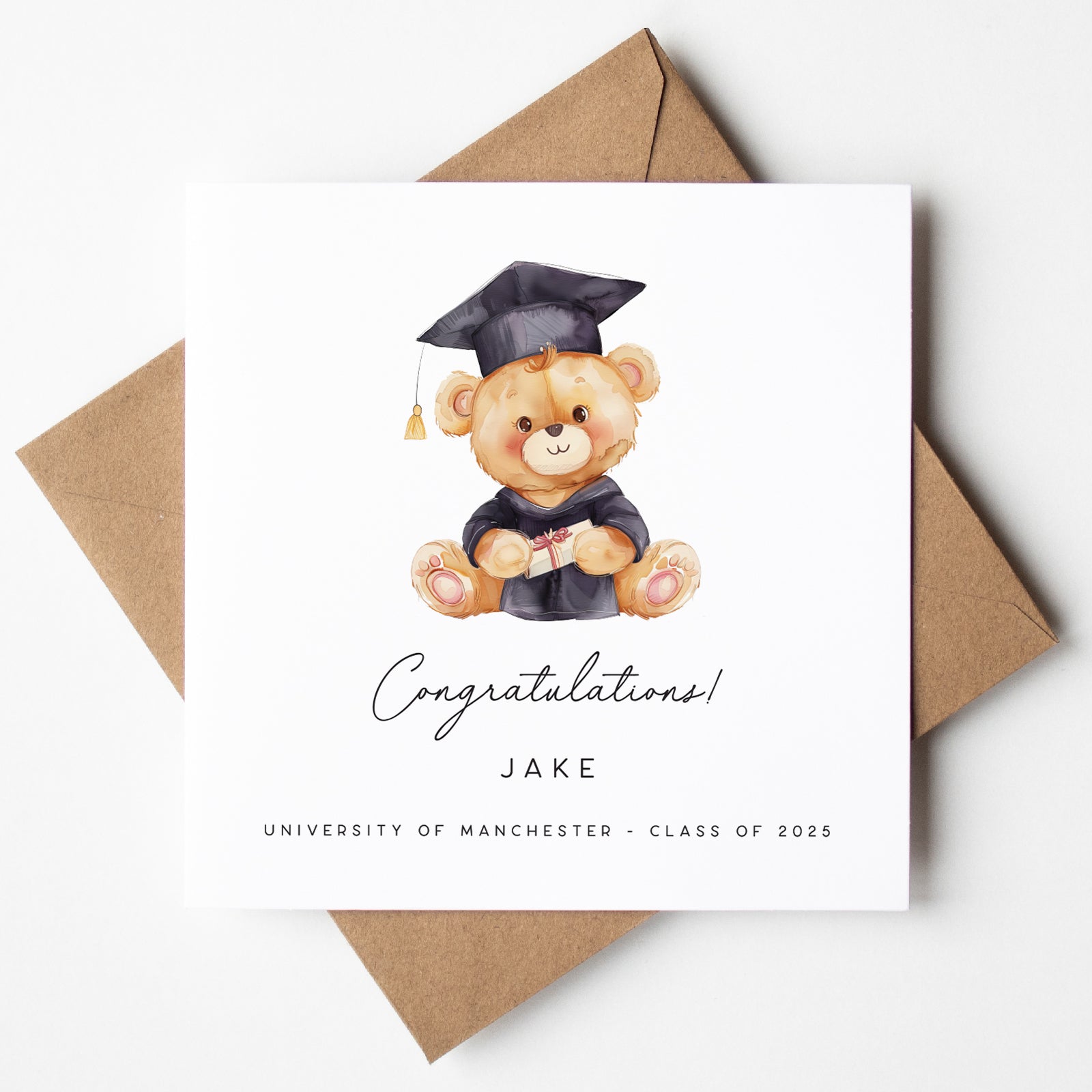 Graduation-themed card with a teddy bear in a cap and gown, surrounded by brown envelopes on a white background.