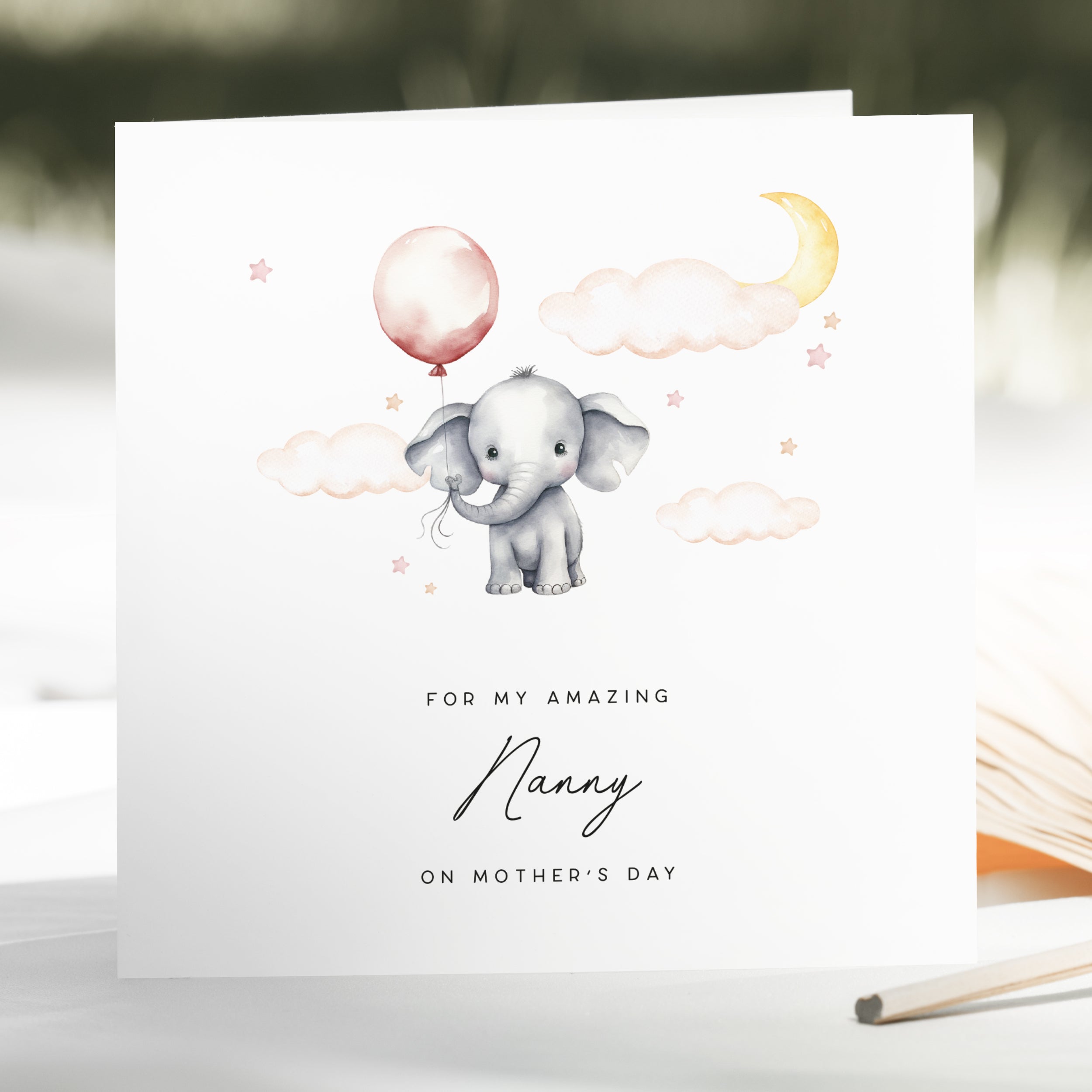 Greeting card with an illustration of a baby elephant holding a pink balloon, surrounded by clouds and stars, on a white background.