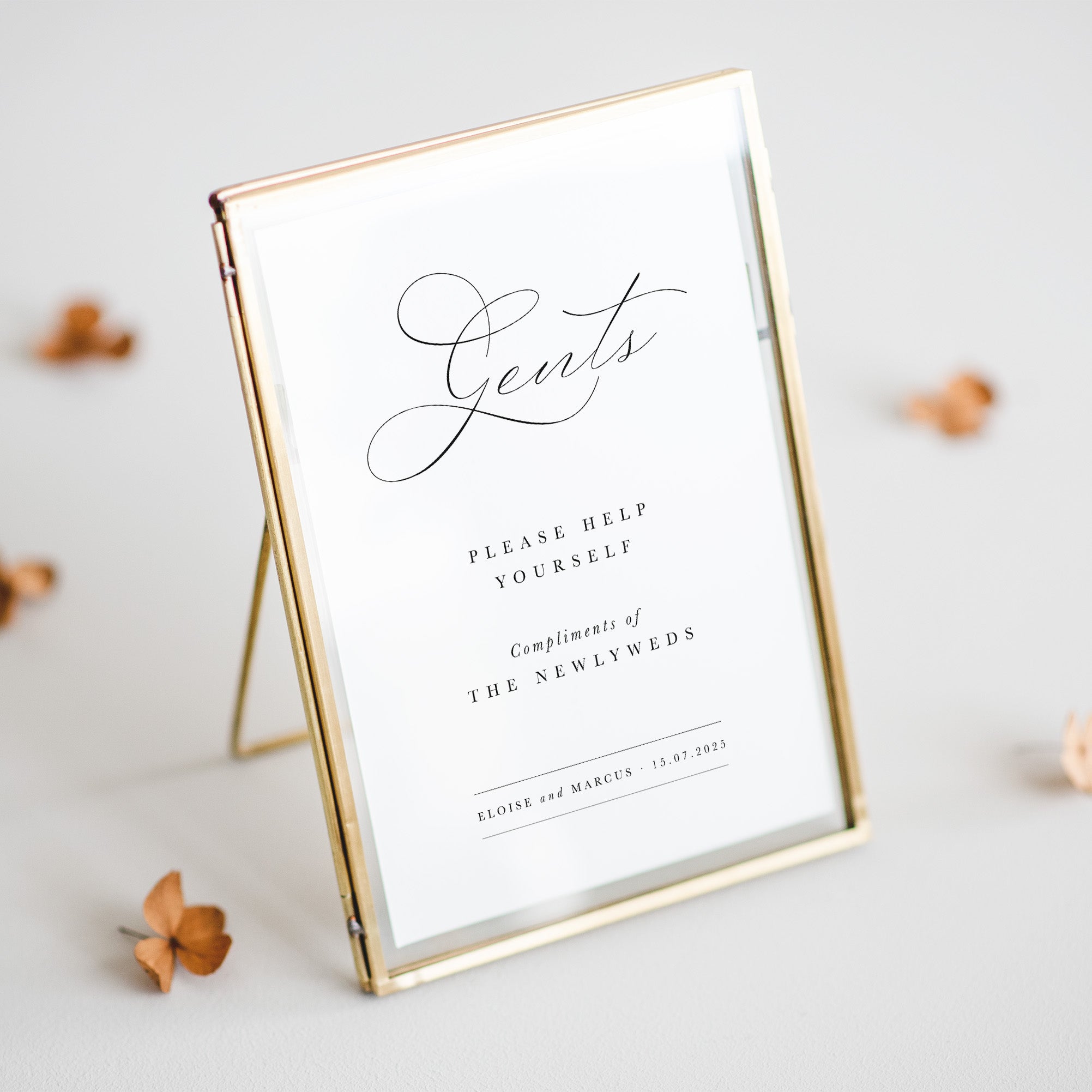 Decorative sign with 'Gents' and wedding details in a gold frame on a light background.