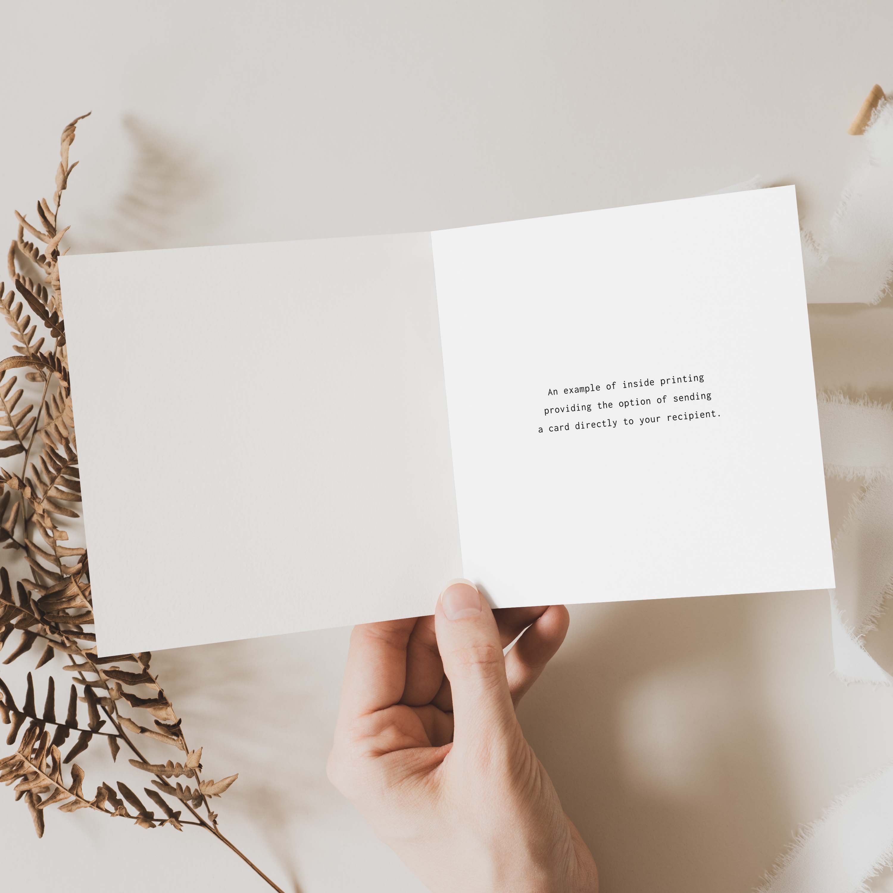Hand holding a white card with text on a light surface with dried leaves.