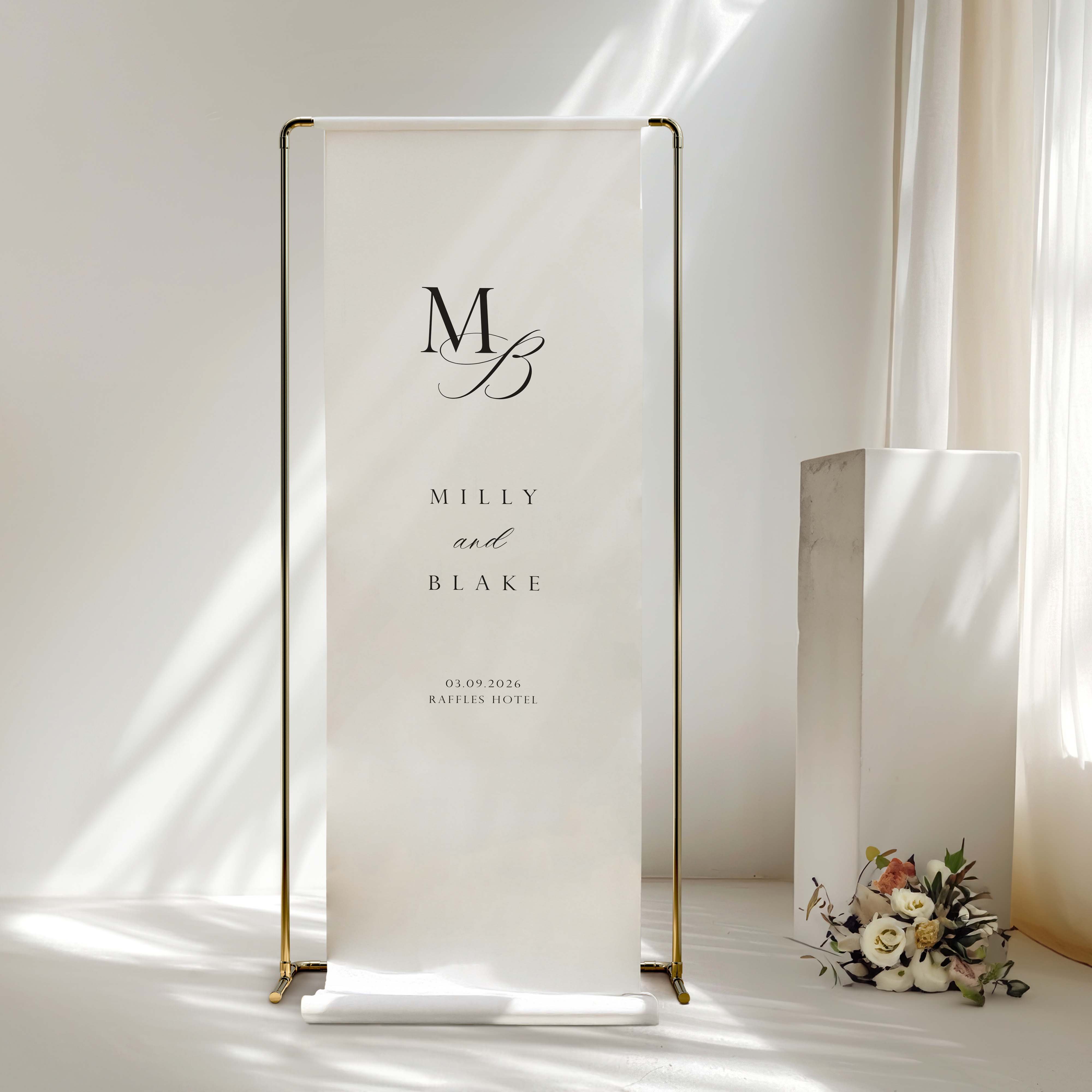 A fabric wedding welcome sign hanging from a gold frame in front of a window.