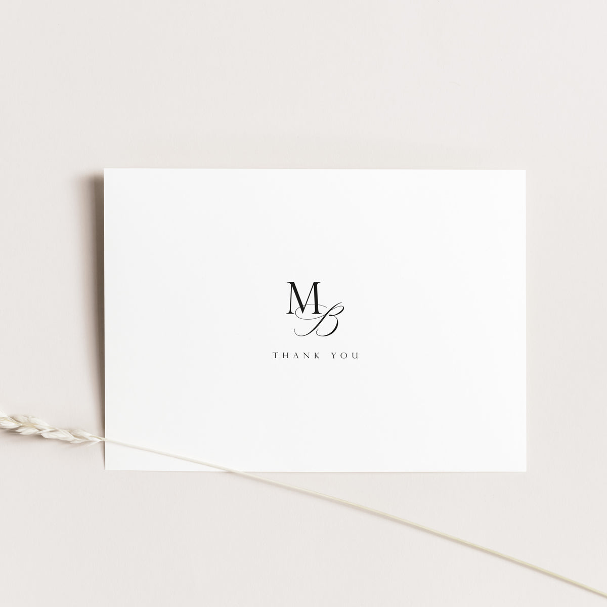A minimalist white thank you card with a black monogram 'MB' and the words 'THANK YOU' printed in the center, styled on a light beige background with a dried wheat stem.