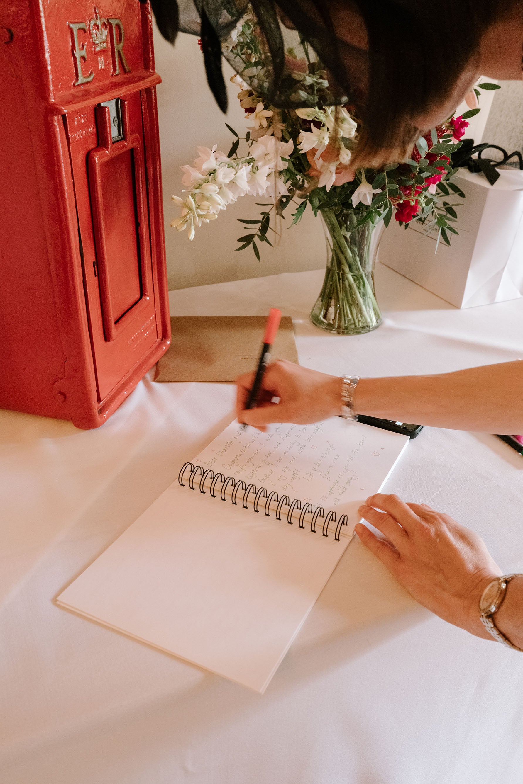 Person writing in a notebook with a red mailbox and flowers in the background