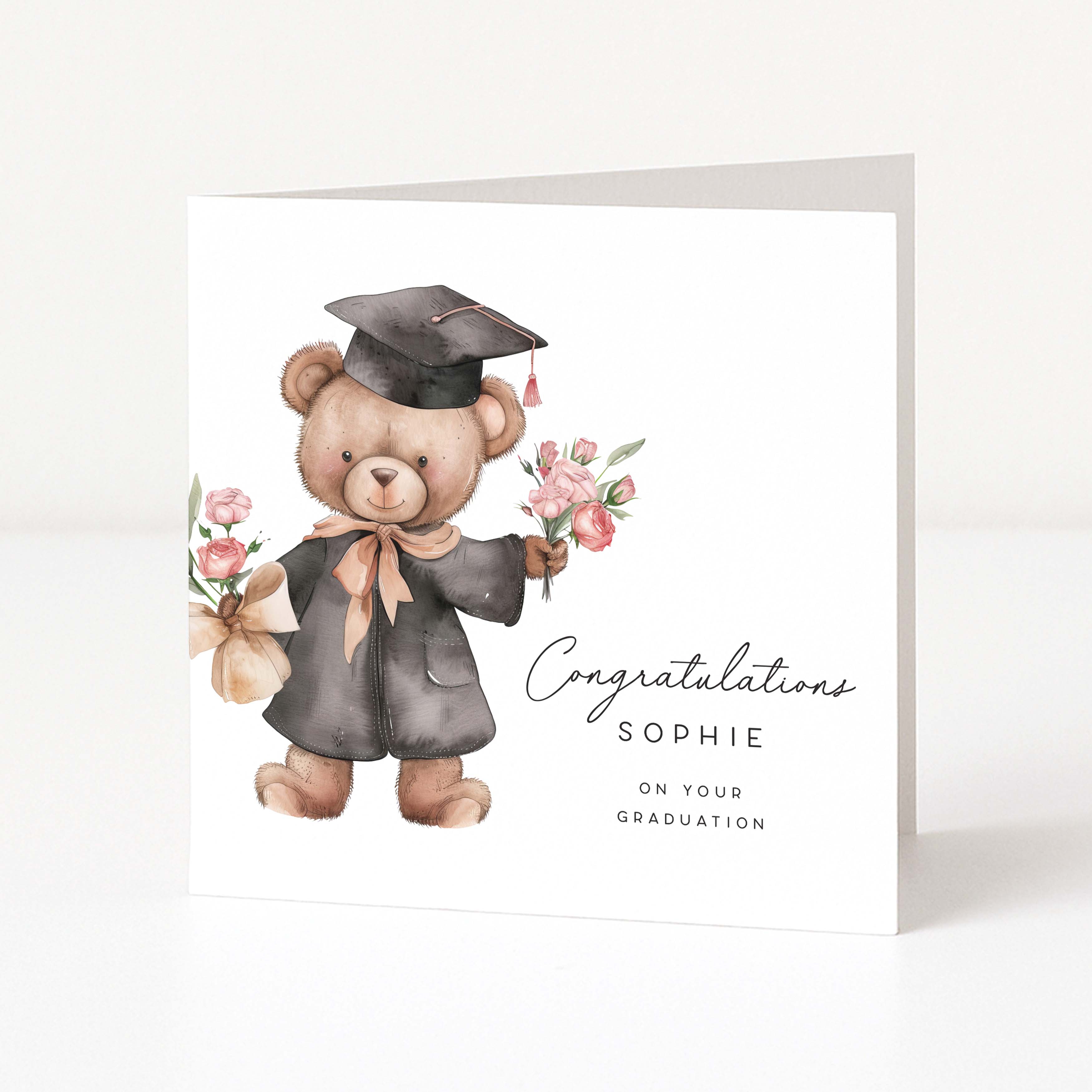Graduation-themed card with a teddy bear holding flowers and a mortarboard hat on a white background.