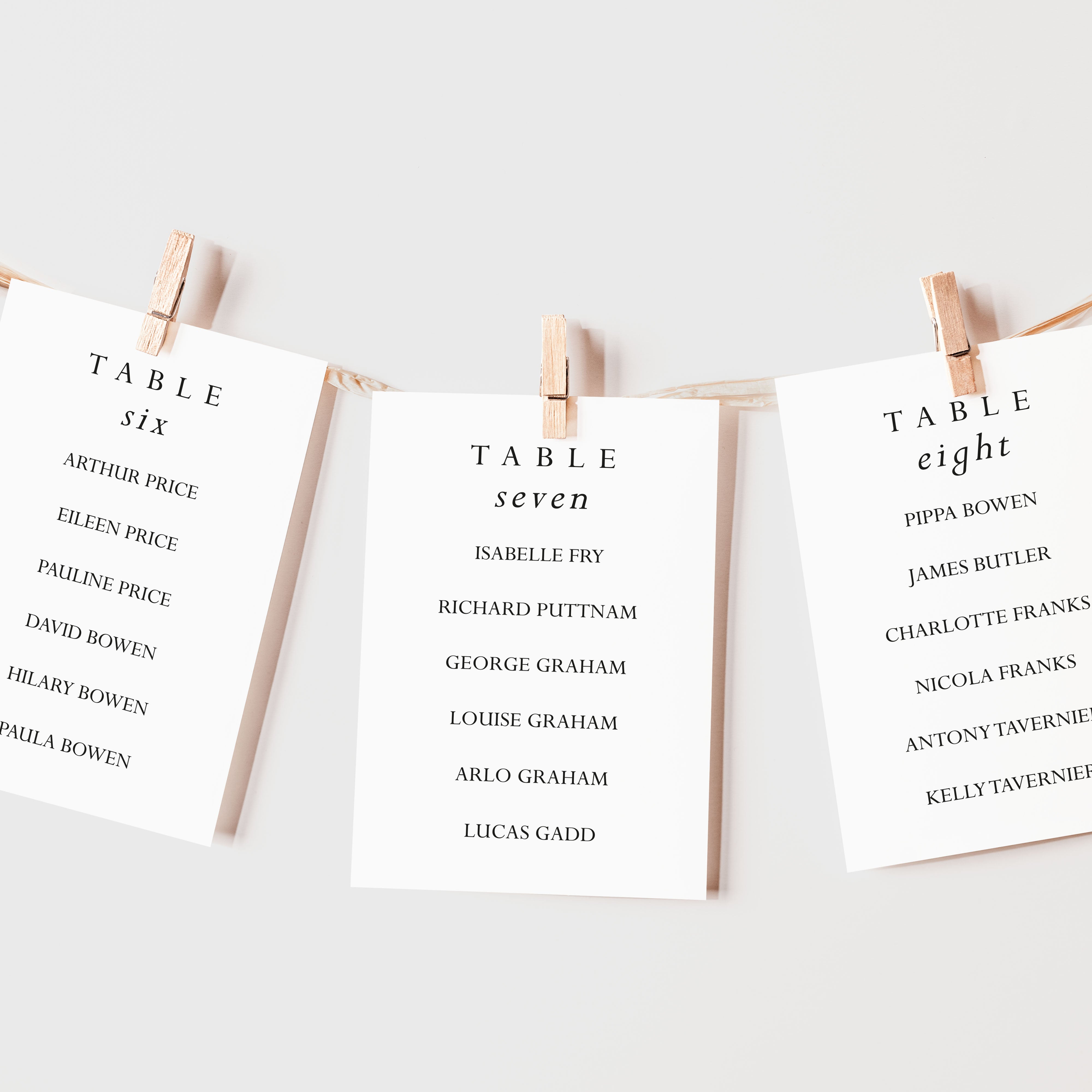 Three white cards with table names and lists of names, pinned to a string on a light background.