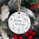Round ornament with 'Happy Holidays' text and floral design, hanging on a tree.