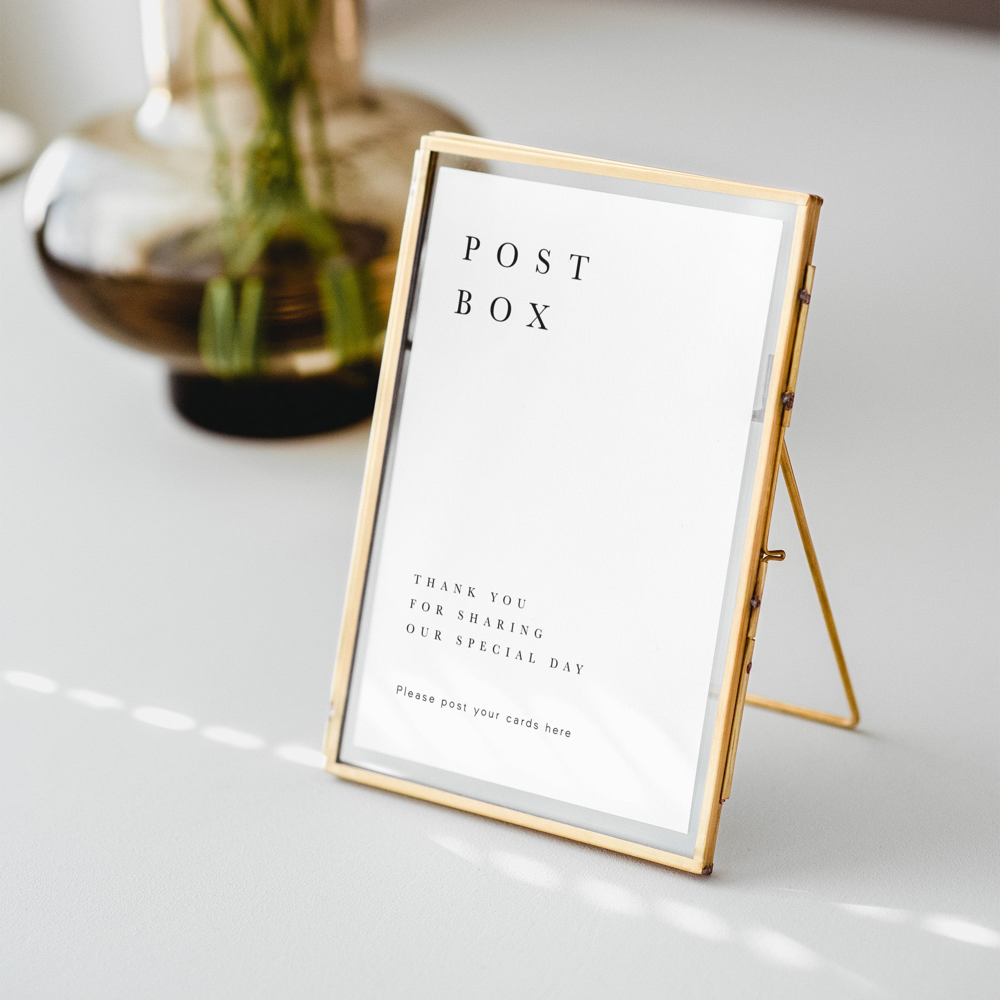 Gold-framed post box sign with a white card inside on a light surface.