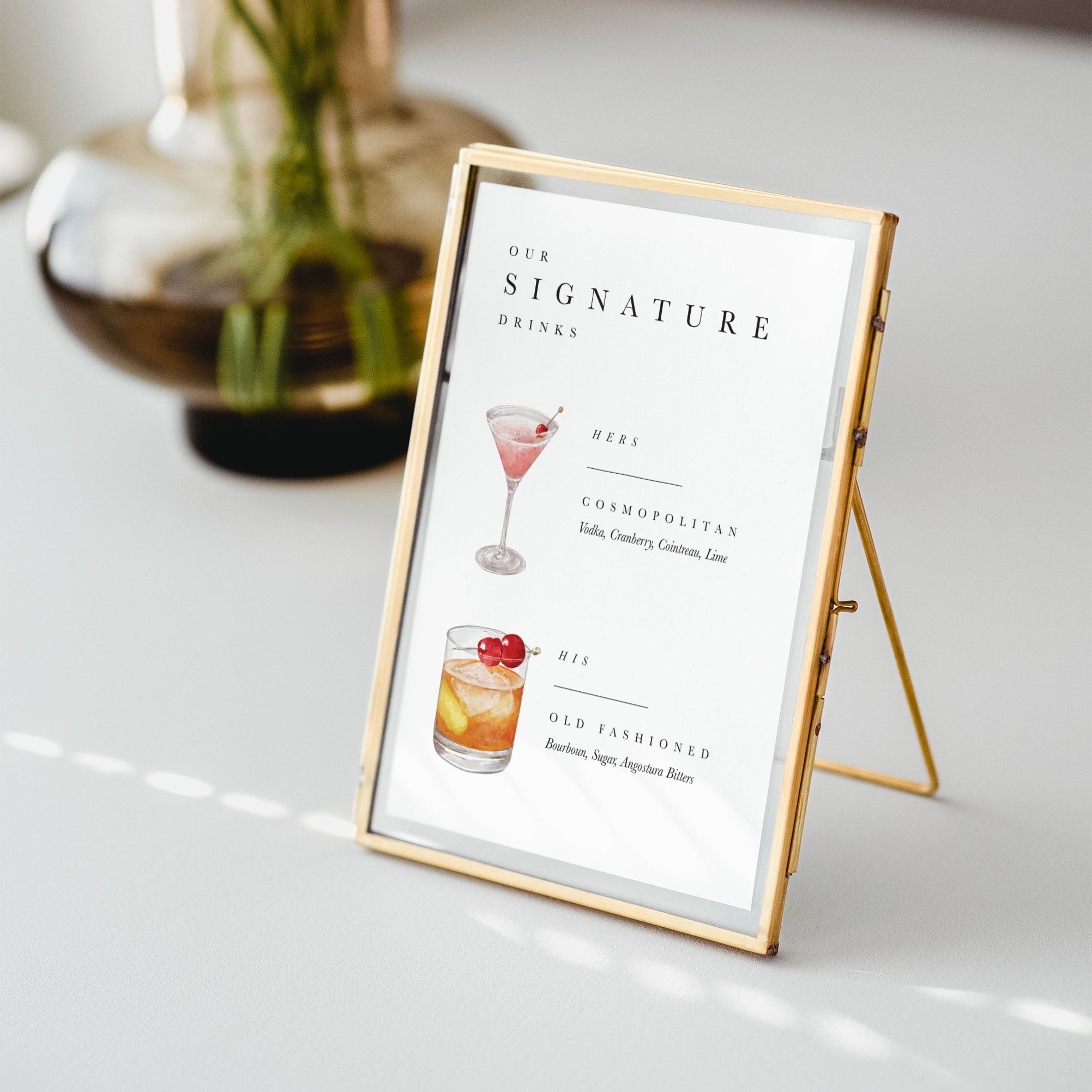 Gold-framed sign with a cocktail menu on a white surface