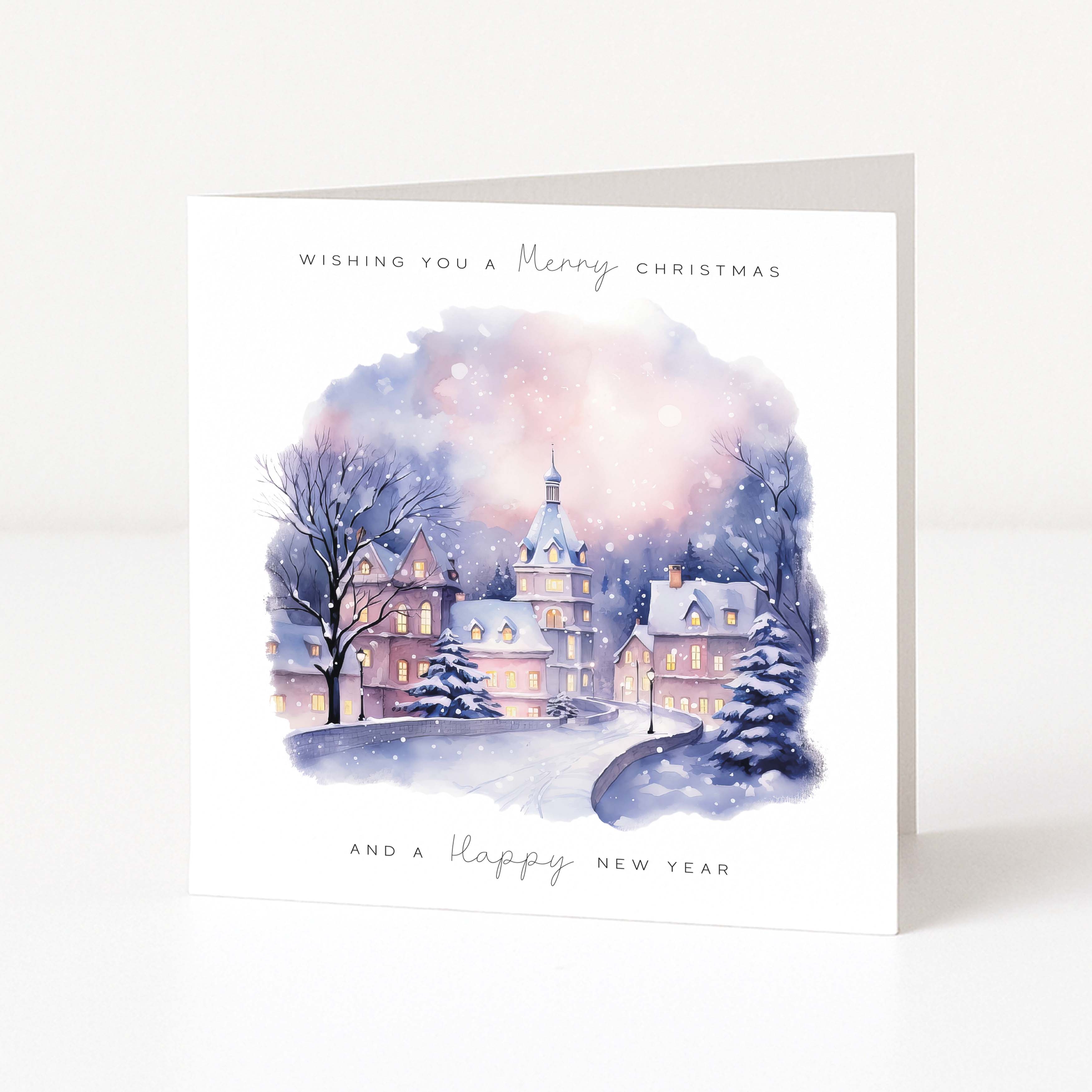A square white greeting card standing upright, printed with a watercolor winter village scene in soft blue, purple, pink, and beige tones. The top reads 'Wishing you a Merry Christmas' and the bottom reads 'And a Happy New Year'.