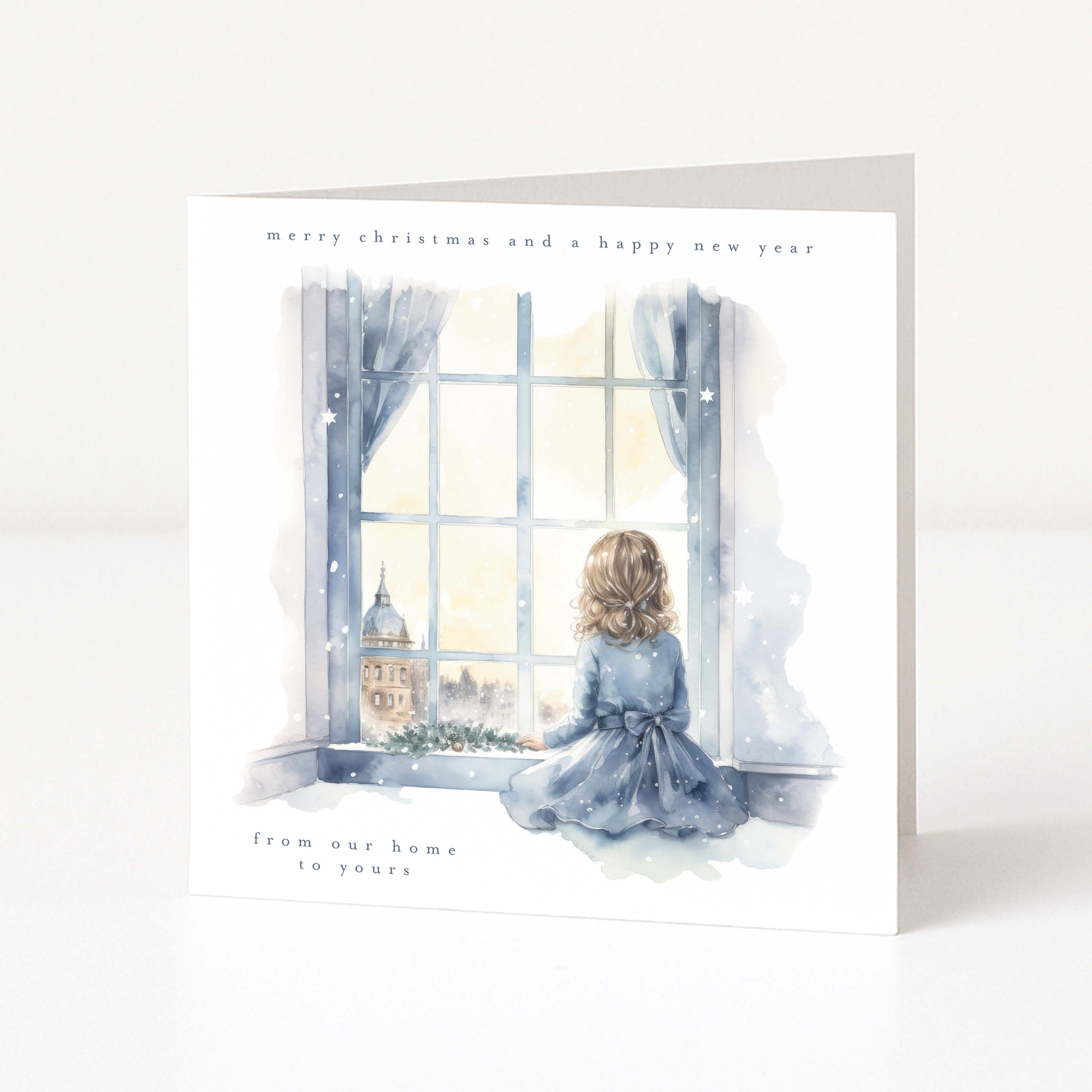 A square Christmas greeting card with a watercolor illustration of a child sitting by a window in winter clothing, looking out at a snowy scene. The card has a white border with the text 'merry christmas and a happy new year' at the top and 'from our home to yours' at the bottom.