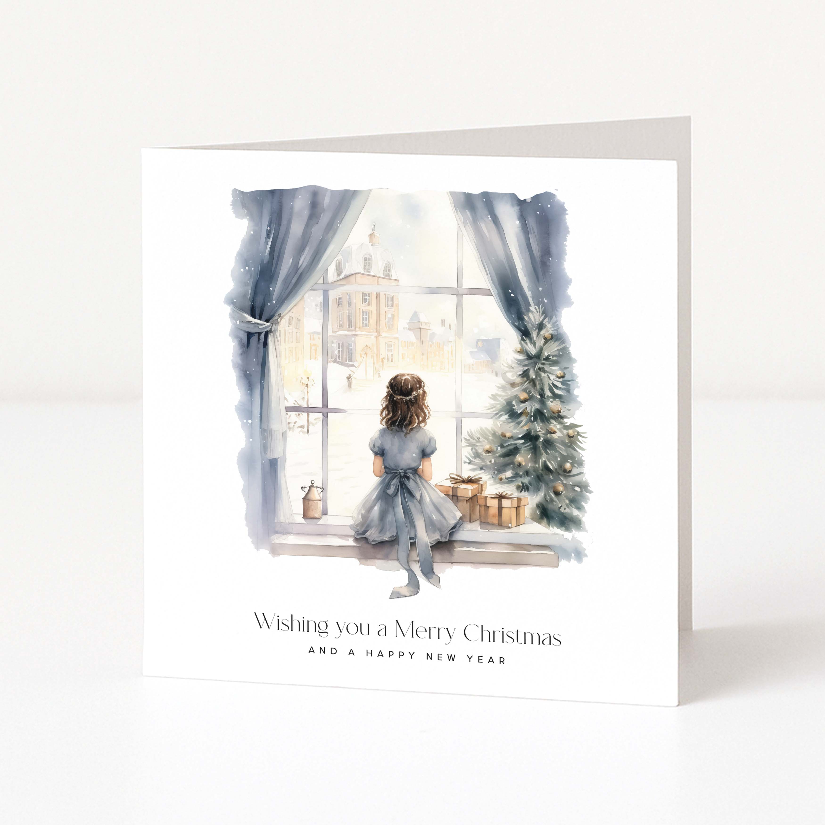 A square white greeting card standing upright on a light gray surface. The front features a watercolor illustration of a girl sitting by a window next to a decorated Christmas tree, with the text 'Wishing you a Merry Christmas AND A HAPPY NEW YEAR' below.