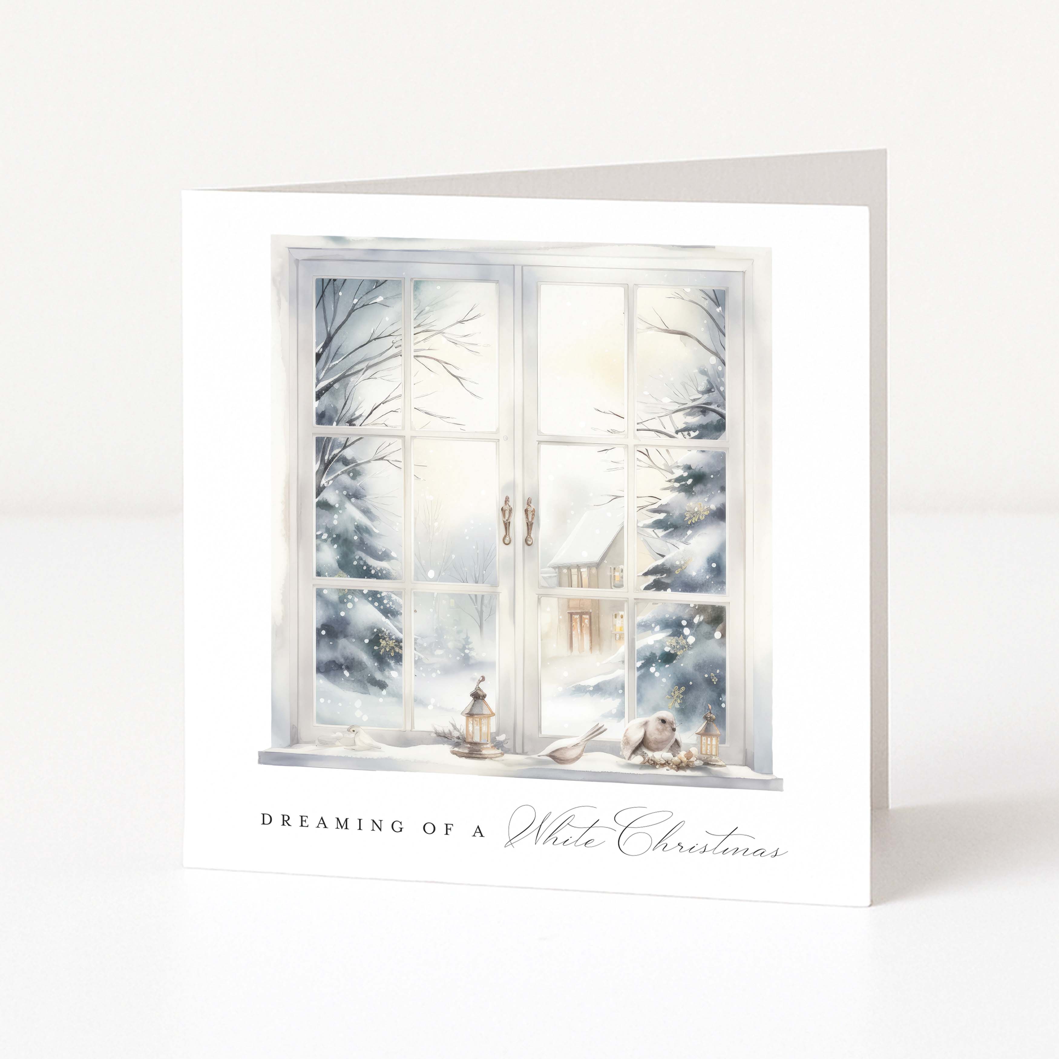 A square white greeting card standing upright, printed with an illustration of a snowy window scene and the text 'DREAMING OF A White Christmas' near the bottom.