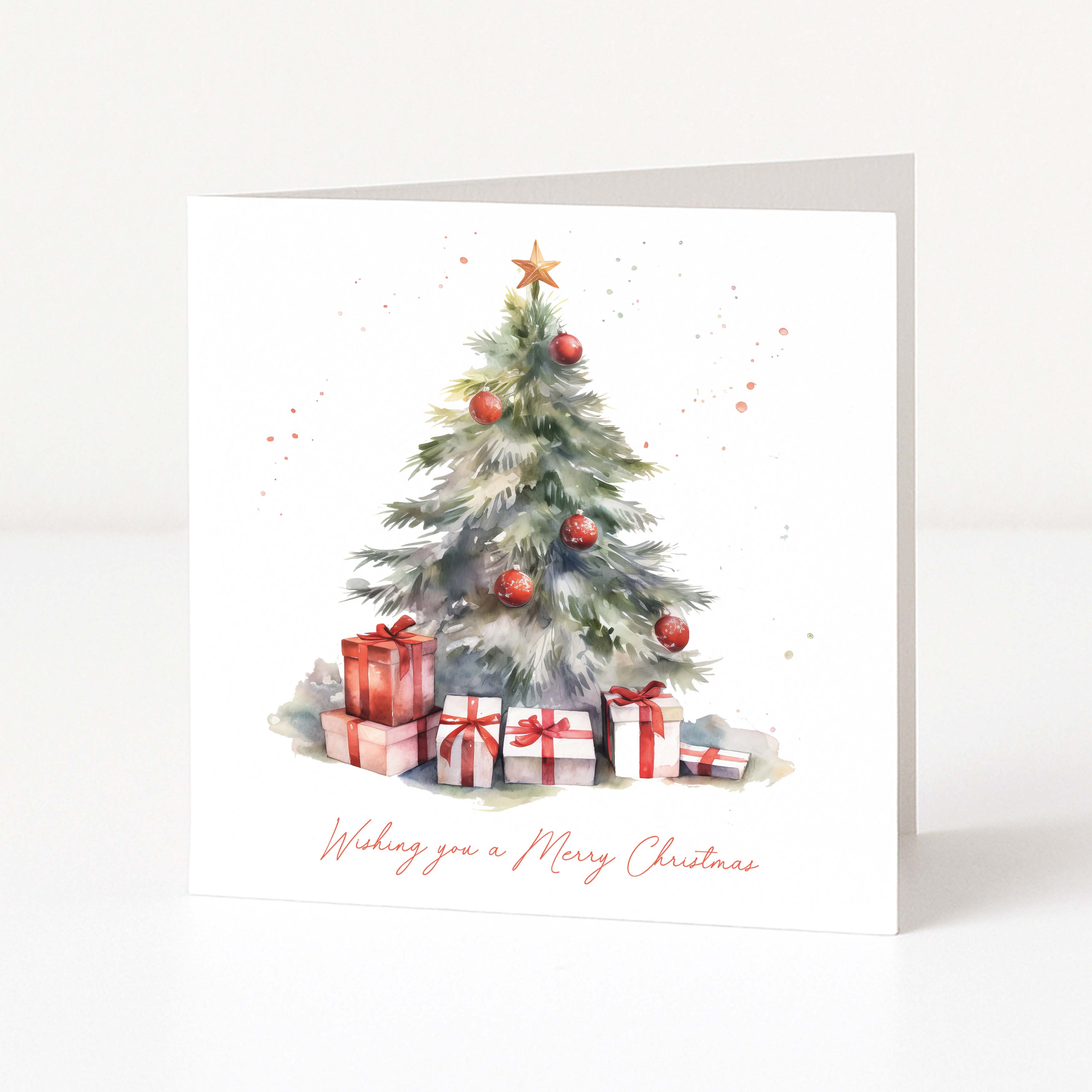 A square white Christmas greeting card standing upright, printed with a watercolor Christmas tree, red ornaments, wrapped presents, and the phrase 'Wishing you a Merry Christmas' in red script.