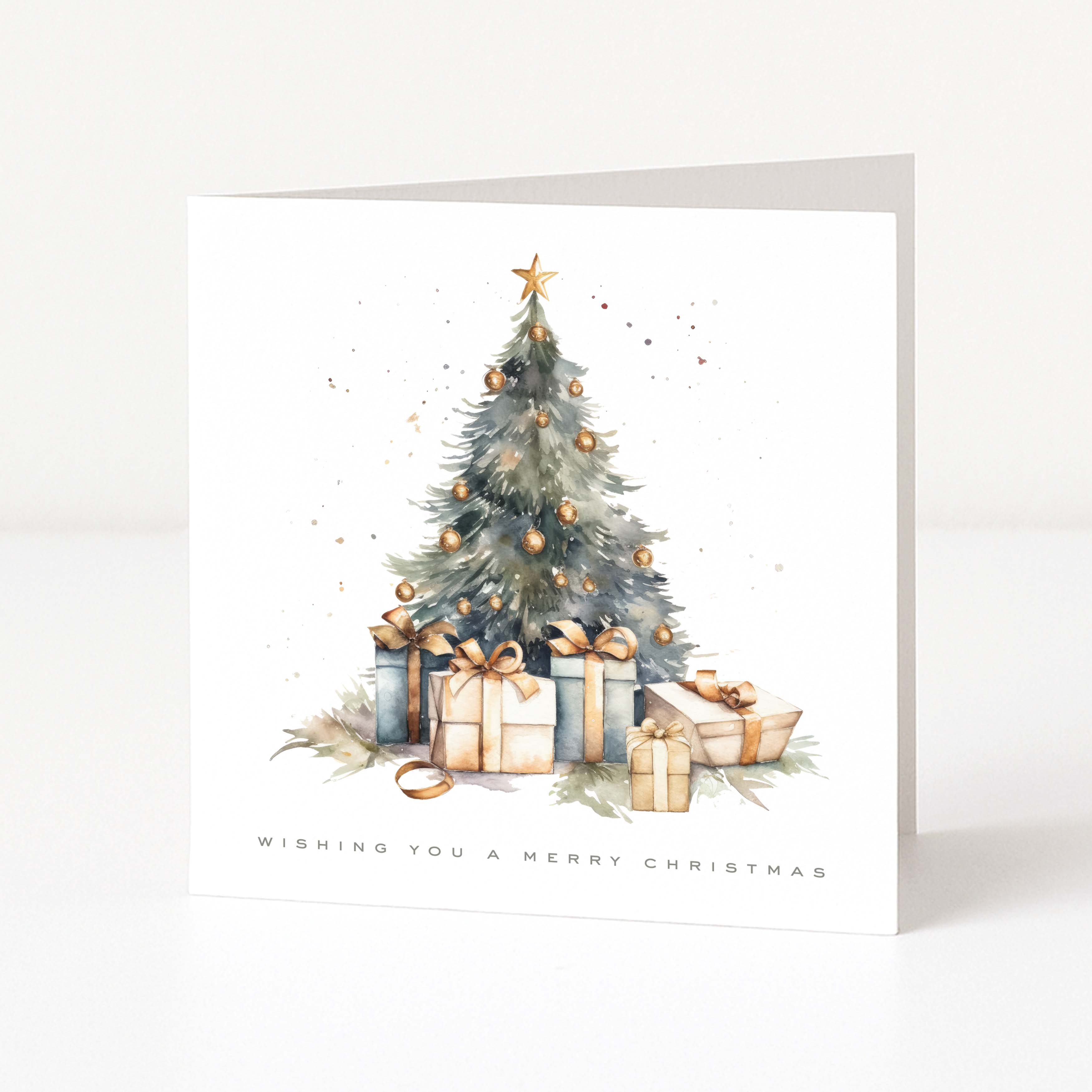 A square Christmas greeting card standing upright on a white surface. The front features a watercolor-style illustration of a decorated Christmas tree with gold ornaments, wrapped gifts, and the text 'WISHING YOU A MERRY CHRISTMAS' at the bottom.