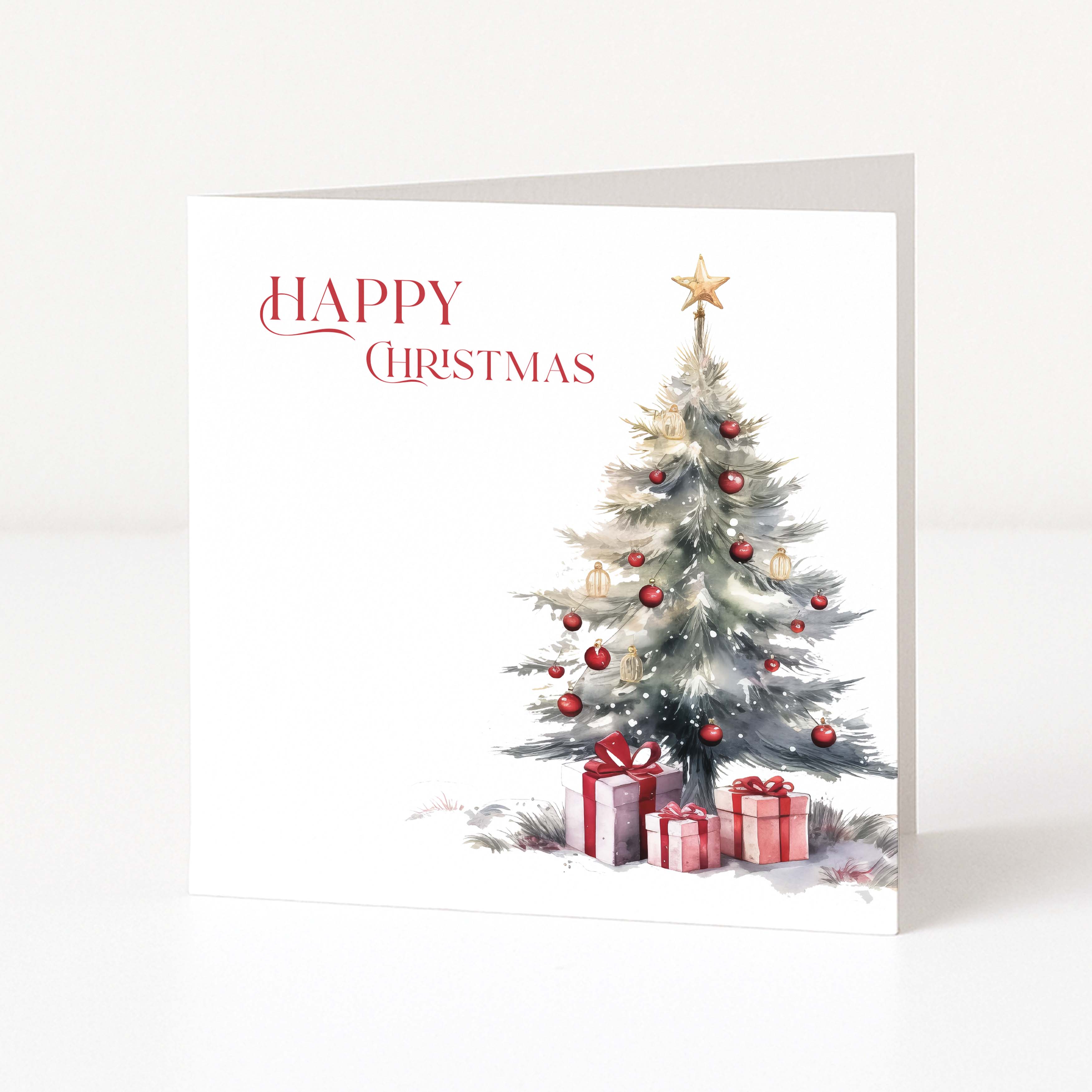 A square Christmas greeting card standing upright on a white surface. The card has a white background with the words 'HAPPY CHRISTMAS' in red script at the upper left and a watercolor-style decorated Christmas tree with red ornaments and wrapped gifts at the lower right.
