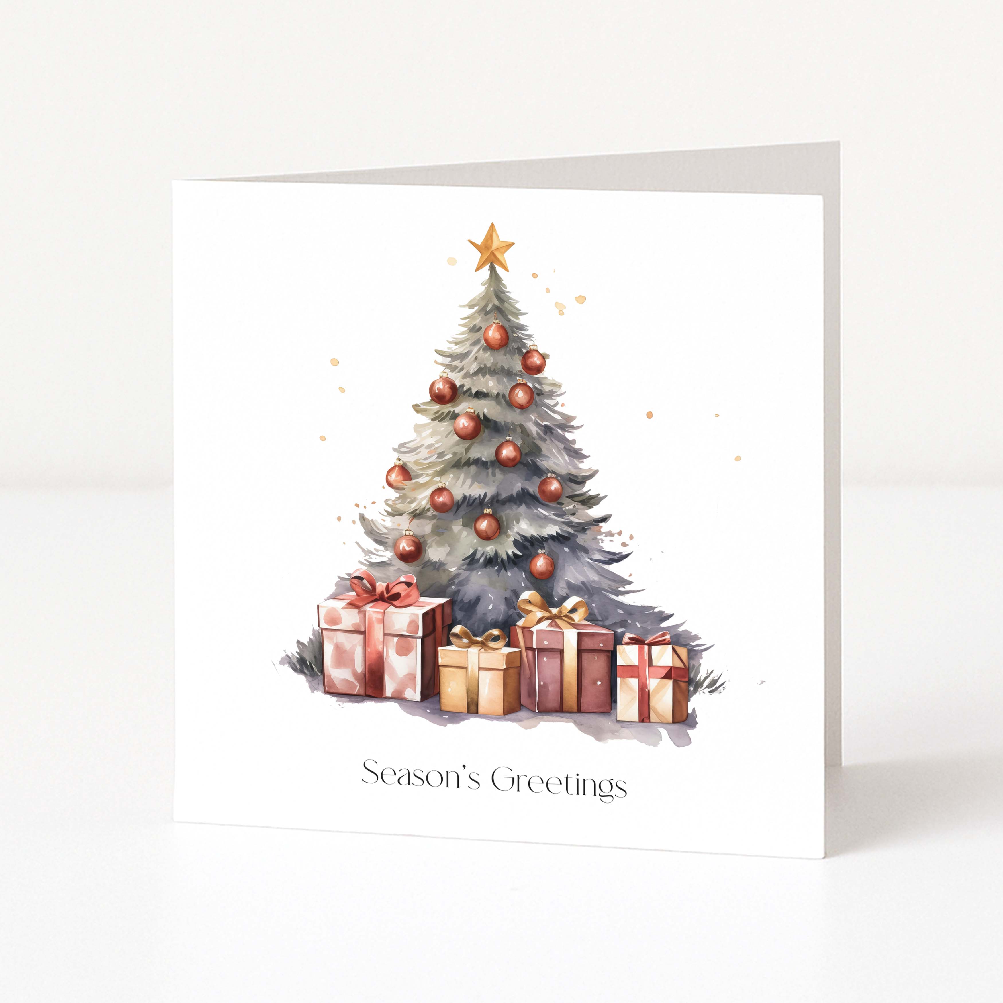 A white Christmas greeting card standing upright, printed with a watercolor-style Christmas tree decorated with gold ornaments and a gold star, with several wrapped presents at the base and the text 'Season's Greetings' near the bottom.