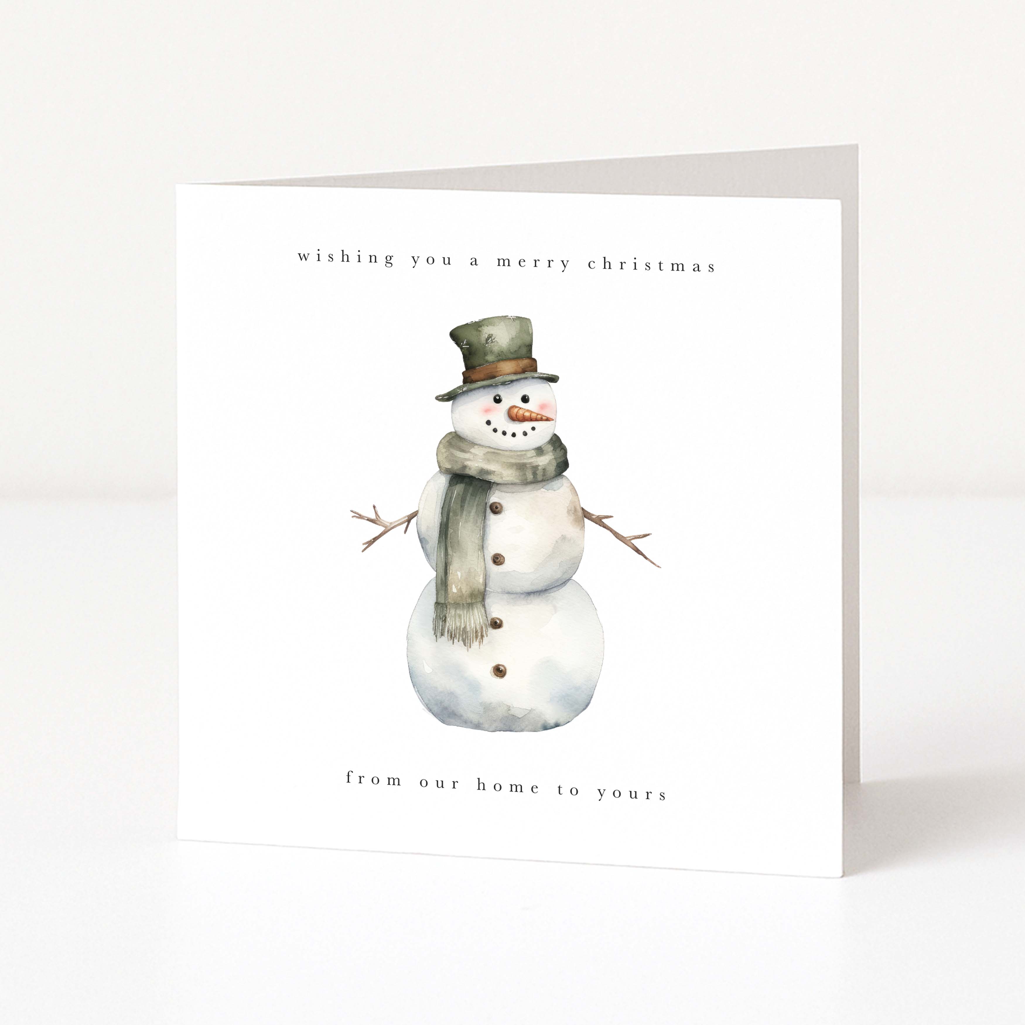 A square white Christmas greeting card standing upright on a white surface. The front features a watercolor-style snowman wearing a dark green top hat and a gray-green scarf, with small black text reading 'wishing you a merry christmas' at the top and 'from our home to yours' at the bottom.