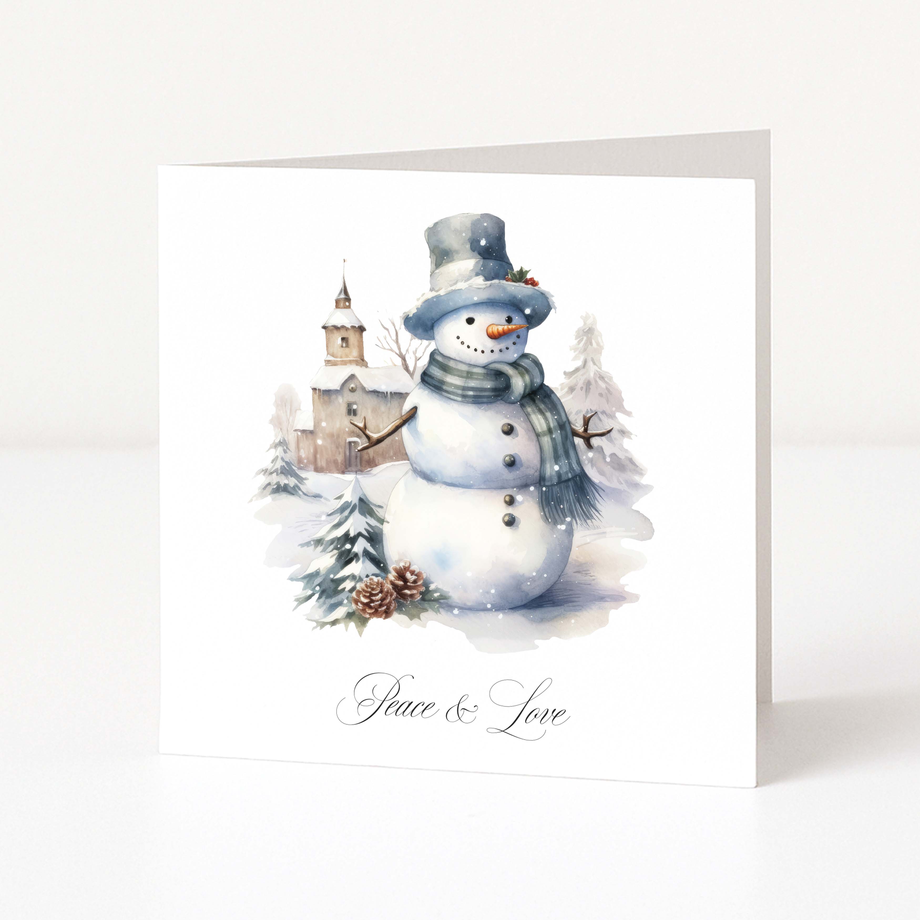 A square white Christmas greeting card standing upright on a white surface, featuring a watercolor illustration of a snowman wearing a top hat and scarf with snowy trees and a small building in the background. The card is printed with the words 'Peace & Love' in black script at the bottom.