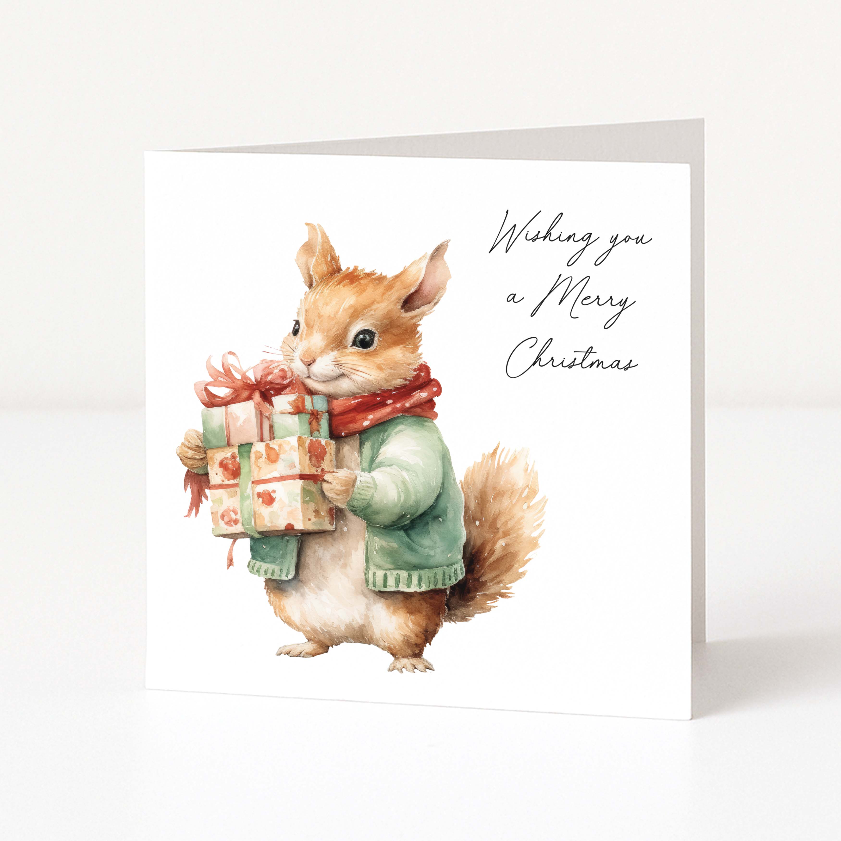 A square Christmas greeting card featuring a watercolour illustration of a squirrel wearing a green sweater and red scarf while holding a wrapped gift box. The right side has the text 'Wishing you a Merry Christmas' in black script.
