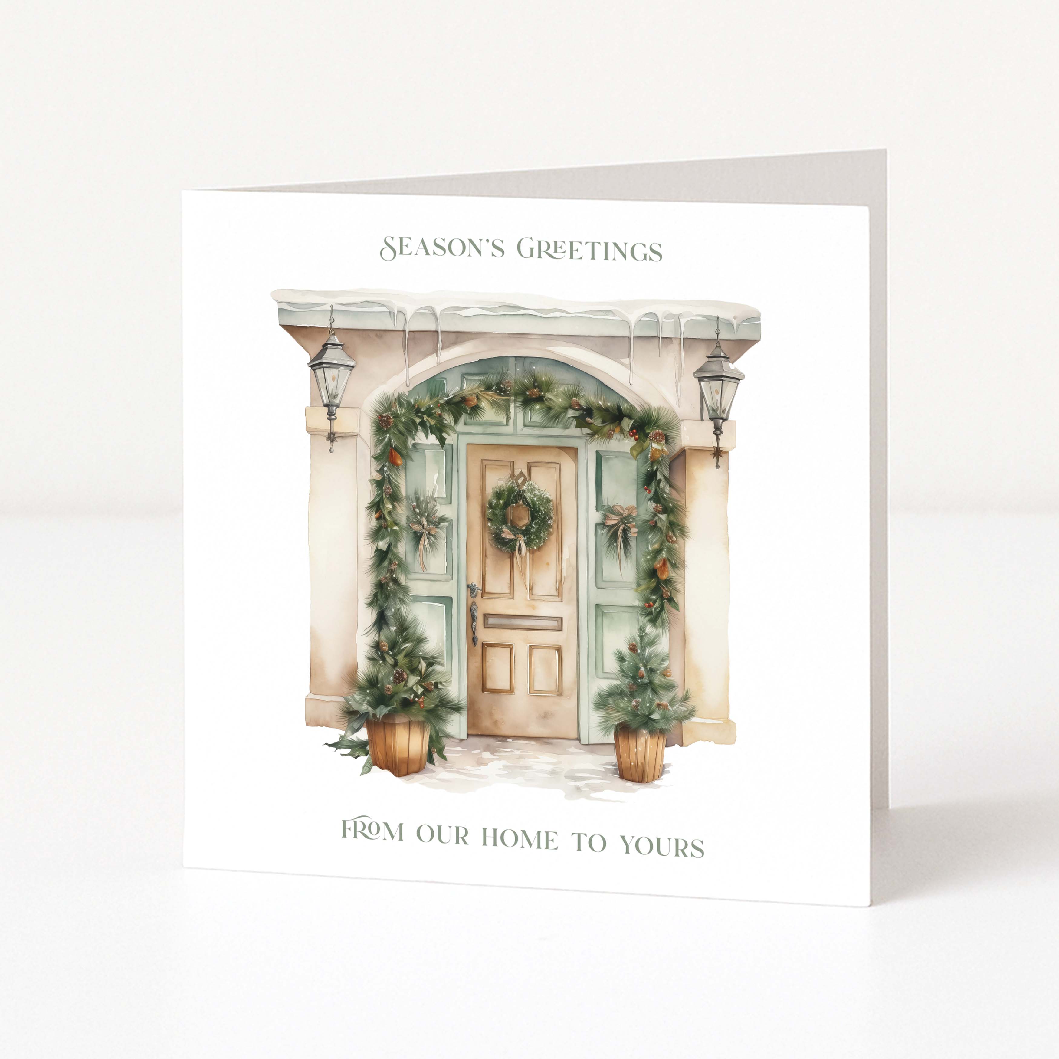 A square white Christmas greeting card standing upright on a white surface, featuring a watercolour-style illustration of a decorated front door with greenery and the text 'SEASON'S GREETINGS' and 'FROM OUR HOME TO YOURS'.