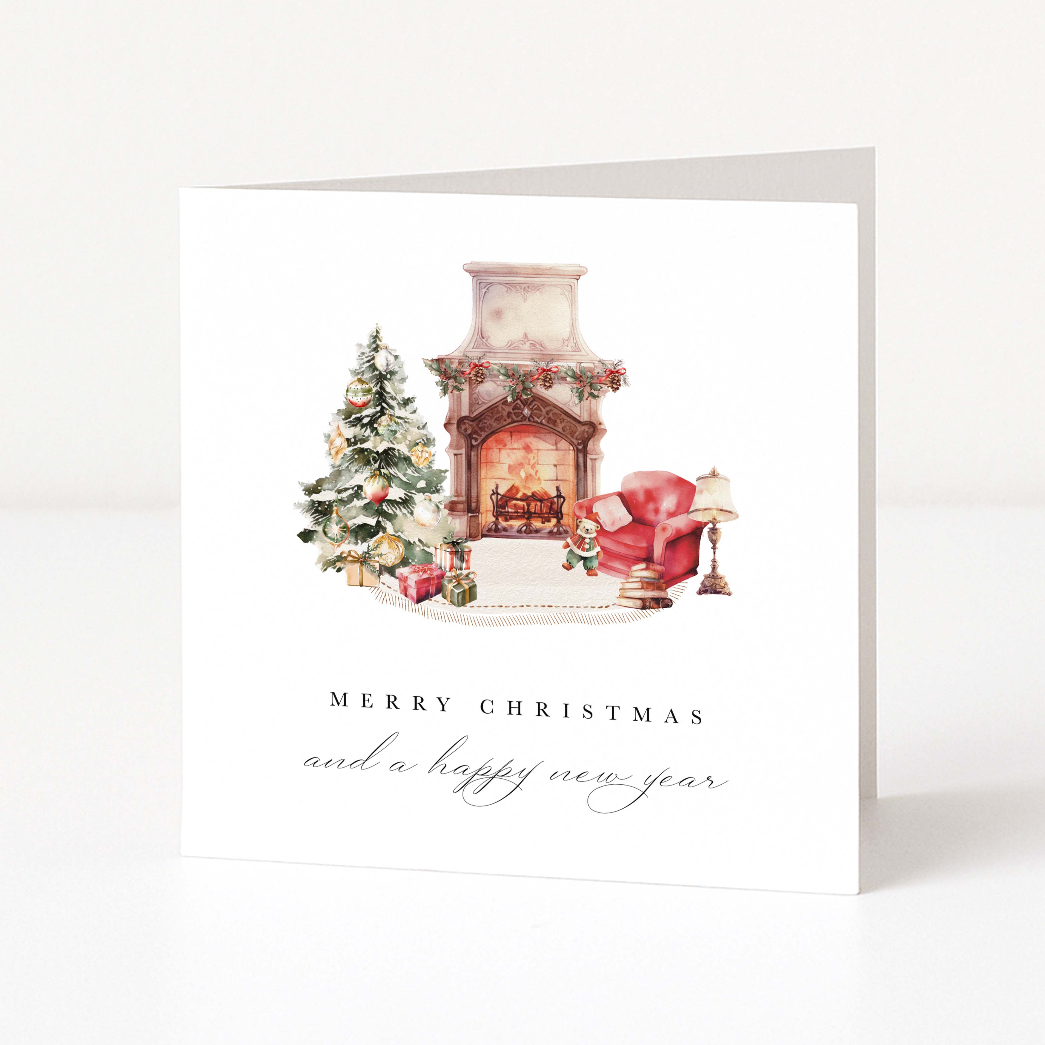 A white Christmas greeting card standing upright, featuring a watercolor illustration of a decorated fireplace, Christmas tree, red armchair, and gifts, with the text 'MERRY CHRISTMAS and a happy new year' below.