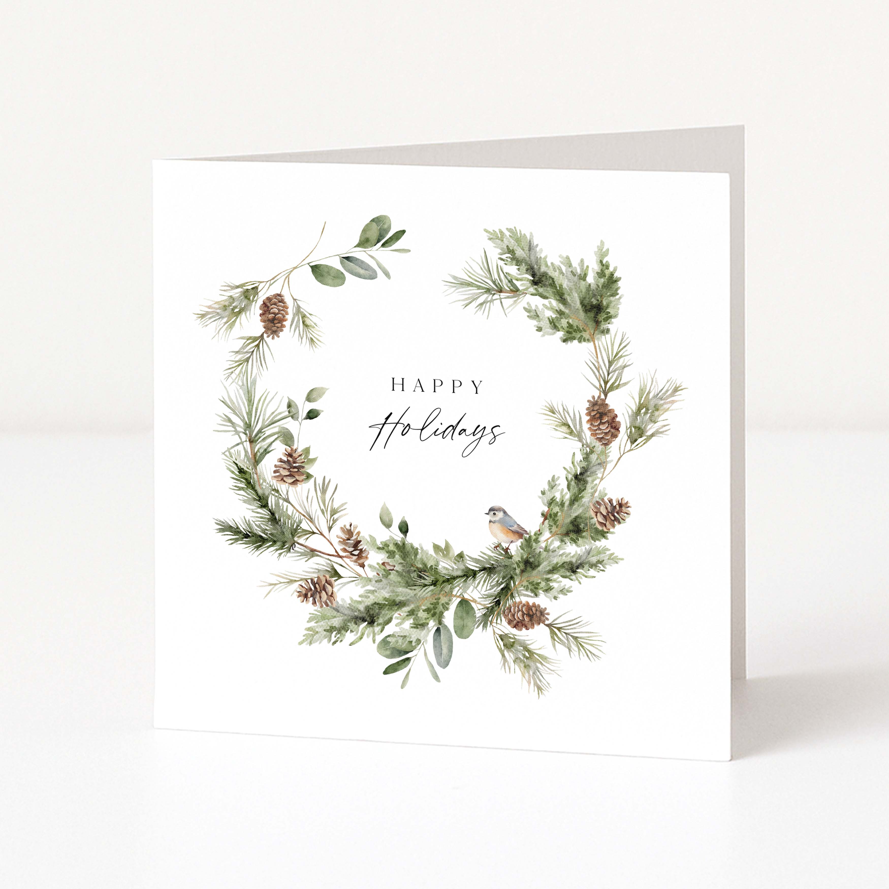 A square white greeting card with a watercolour-style holiday wreath featuring green pine branches, brown pinecones, and a small bird, with the words 'Happy Holidays' centred on a clean white background.