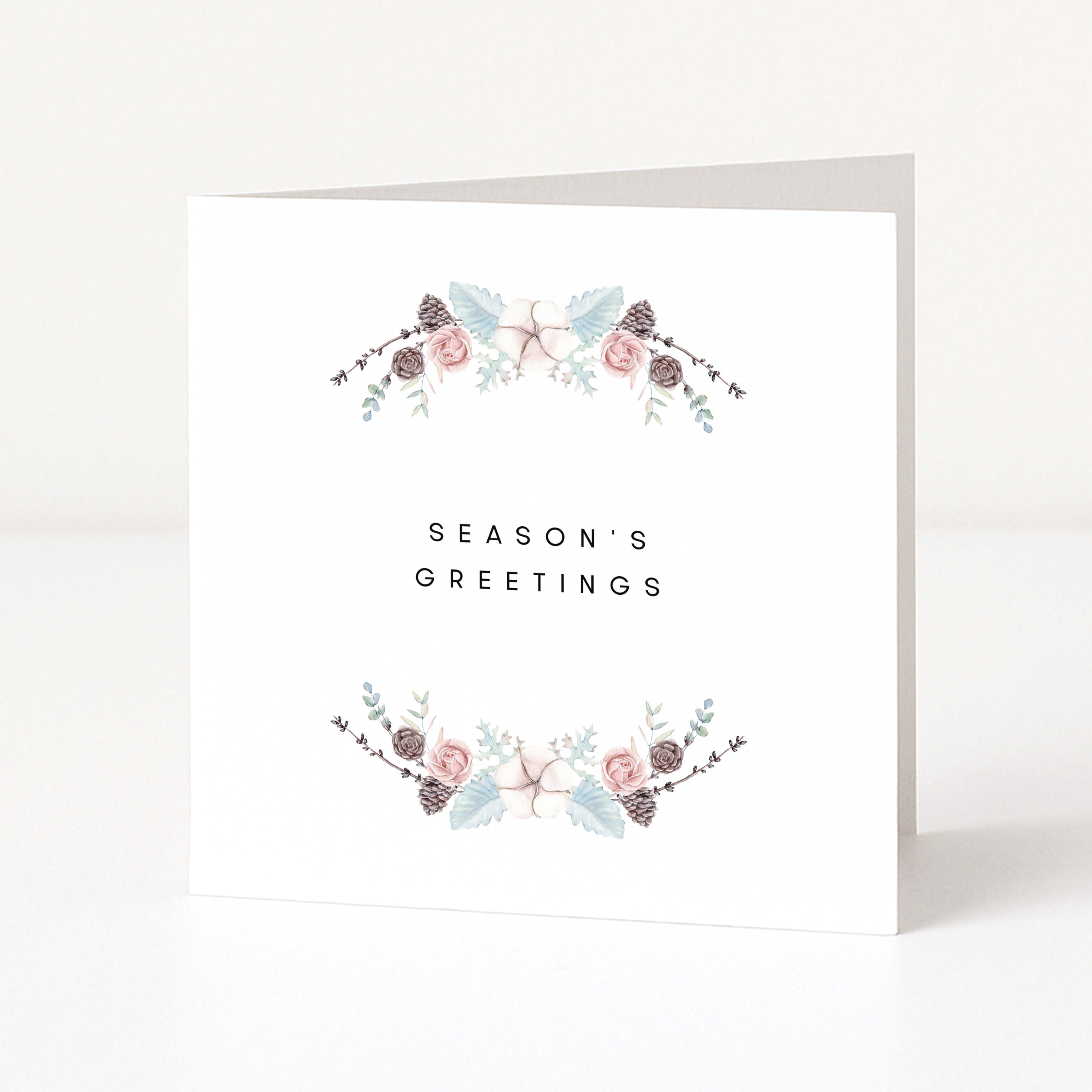 A white Christmas greeting card standing upright on a white surface, with the words 'SEASON'S GREETINGS' centered between two delicate floral garlands in soft pink, sage green, and taupe tones.