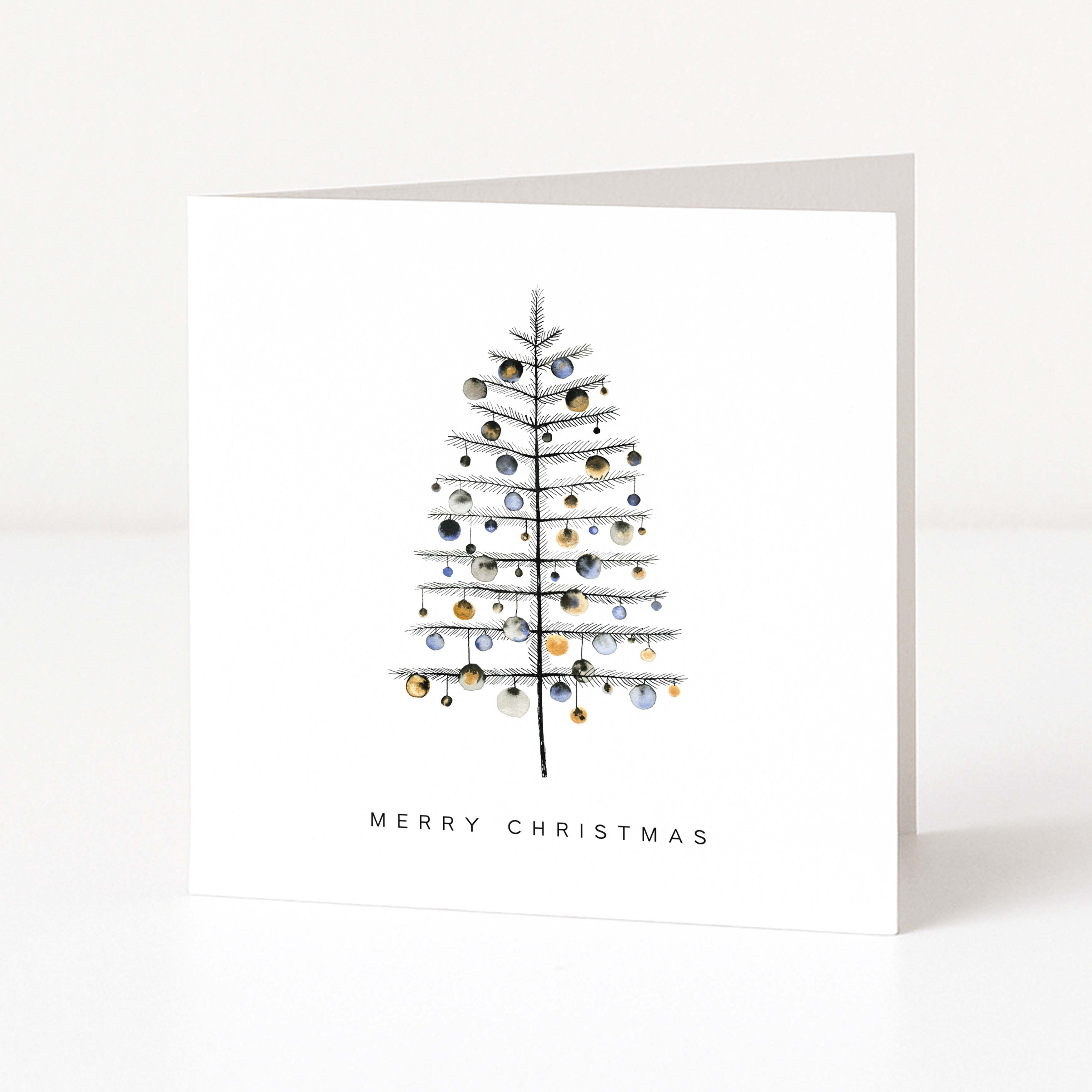 A white square Christmas greeting card standing upright on a white surface, featuring a minimalist black line drawing of a Christmas tree decorated with small metallic gold and silver ornaments, with the text 'MERRY CHRISTMAS' below.