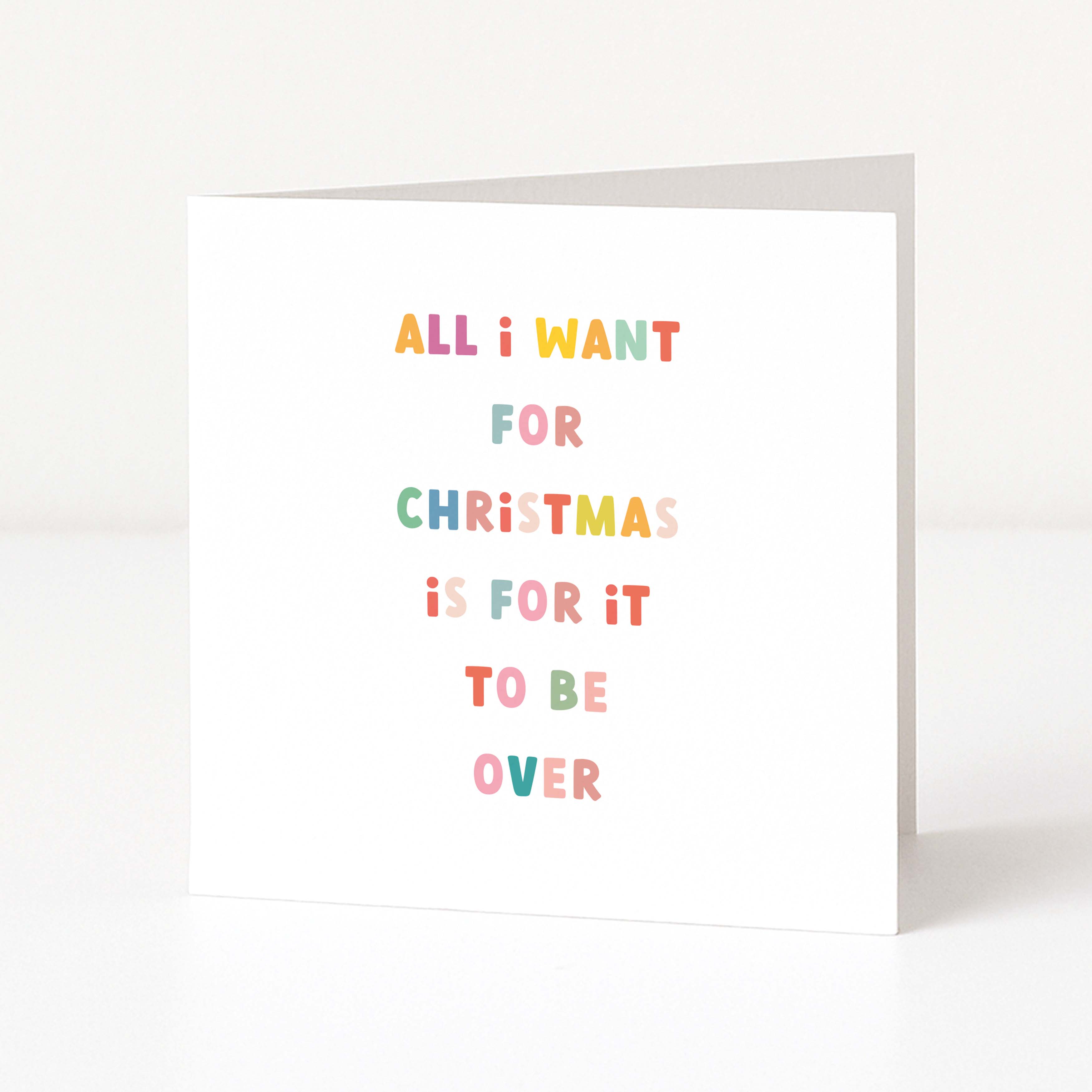A white anti-Christmas card standing upright on a white surface, with colorful text that reads, 'ALL I WANT FOR CHRISTMAS IS FOR IT TO BE OVER.'.