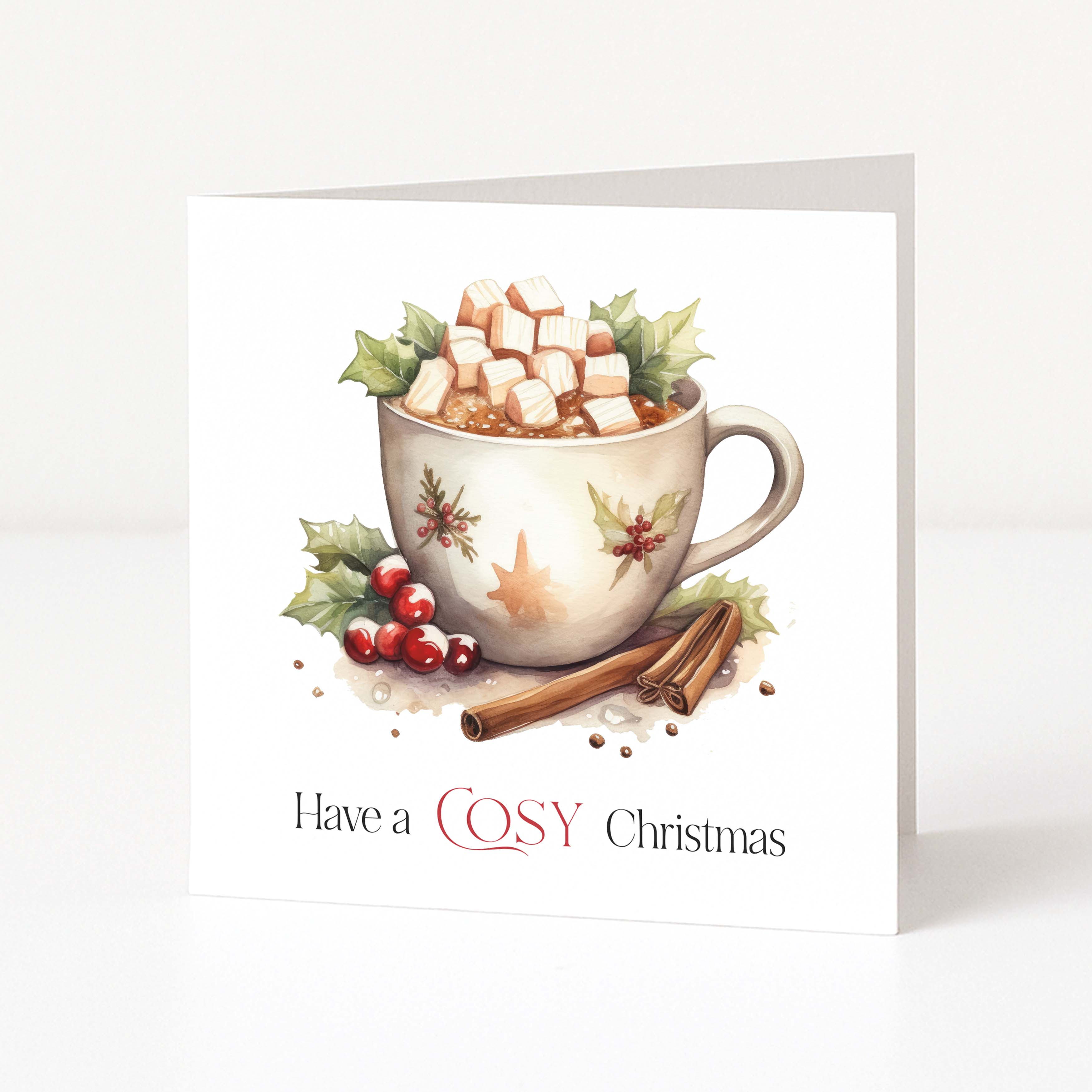 A square Christmas greeting card standing upright on a white surface. The front features an illustration of a white mug filled with hot chocolate, marshmallows, and holly leaves, with cinnamon sticks and the text 'Have a COSY Christmas' printed below.