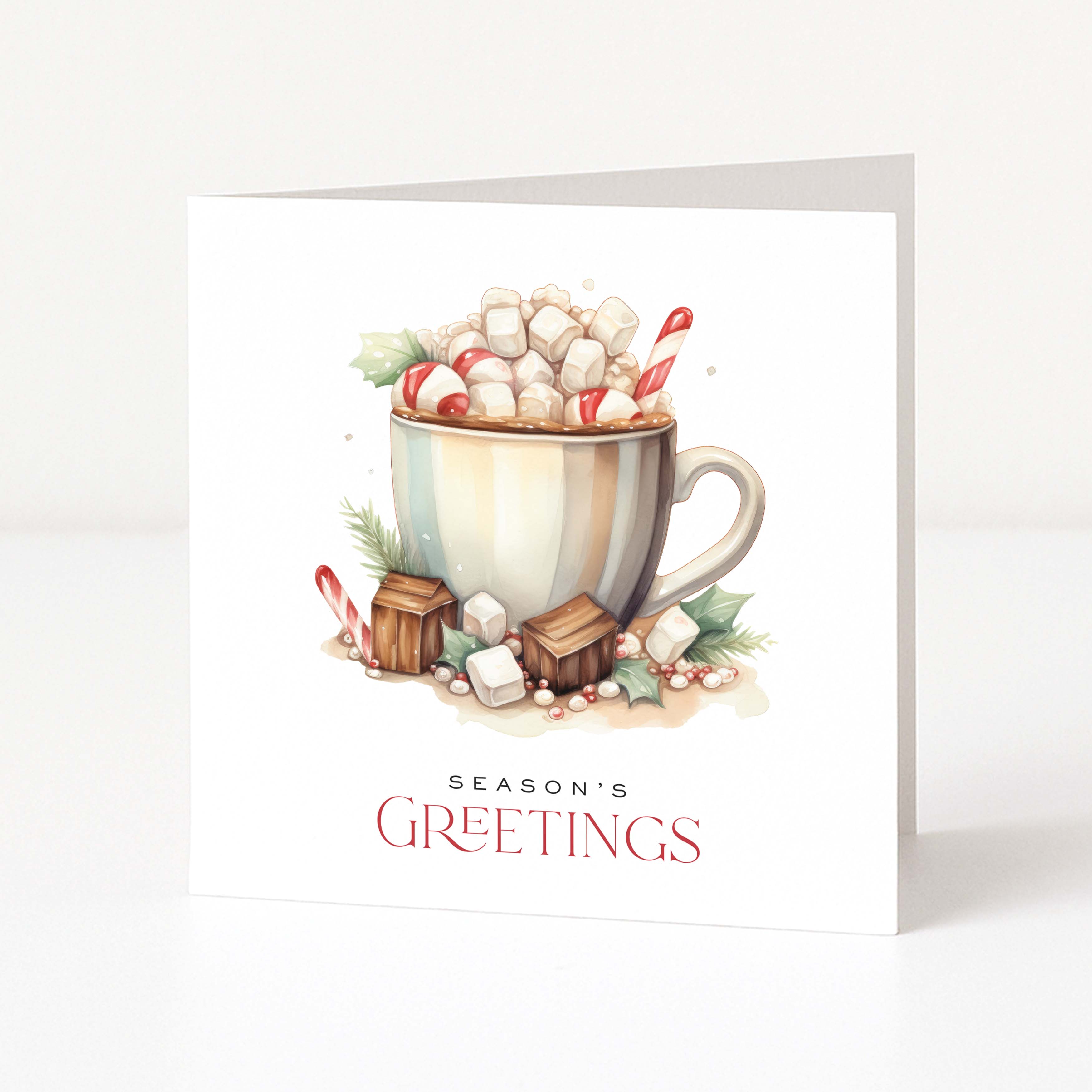 A white Christmas greeting card standing upright, featuring an illustrated hot chocolate mug topped with marshmallows, candy canes, and greenery, with the text 'SEASON'S GREETINGS' below.