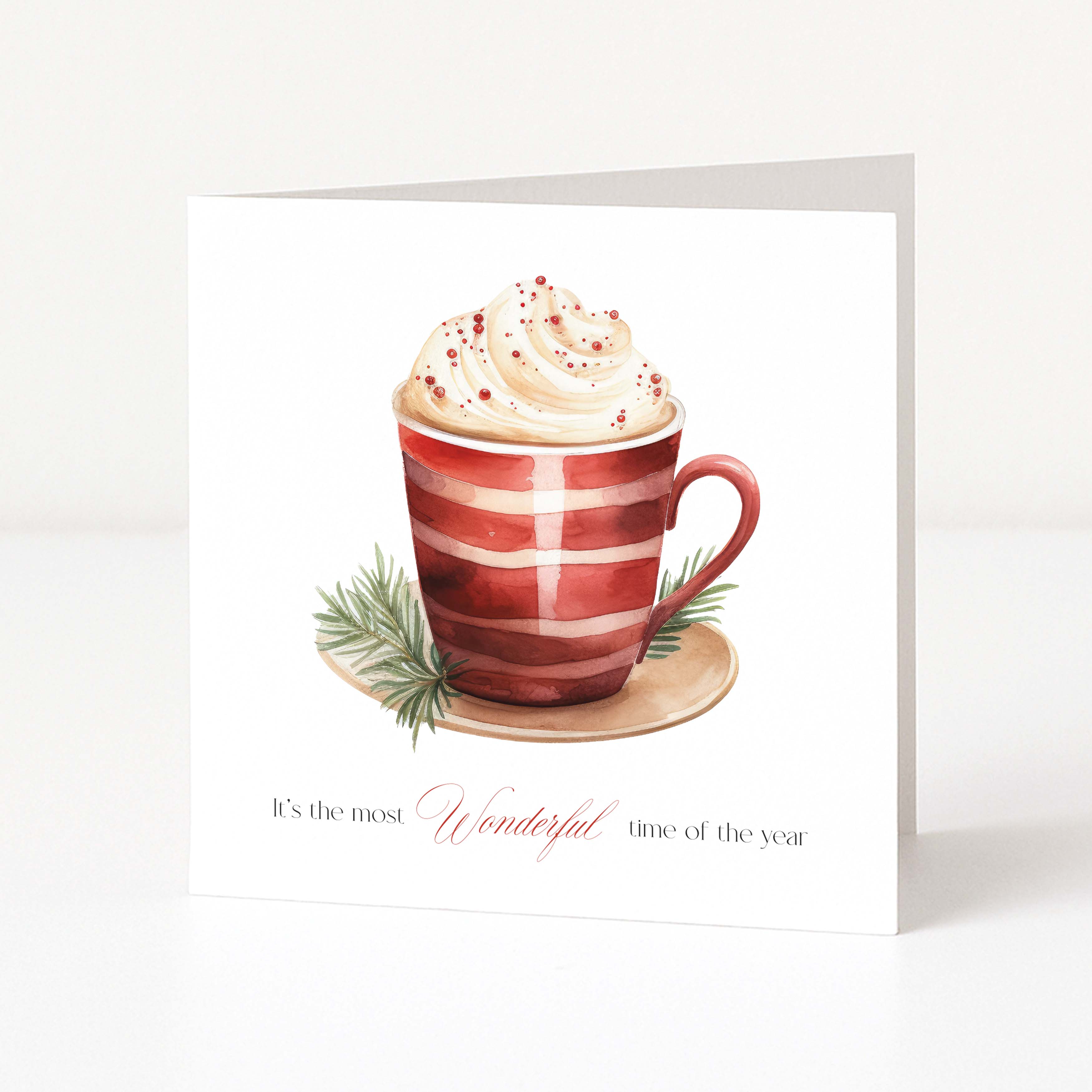 A square Christmas greeting card featuring a watercolor illustration of a red-and-white striped mug filled with whipped cream and holiday sprigs, with the text 'It's the most Wonderful time of the year' printed below on a white background.