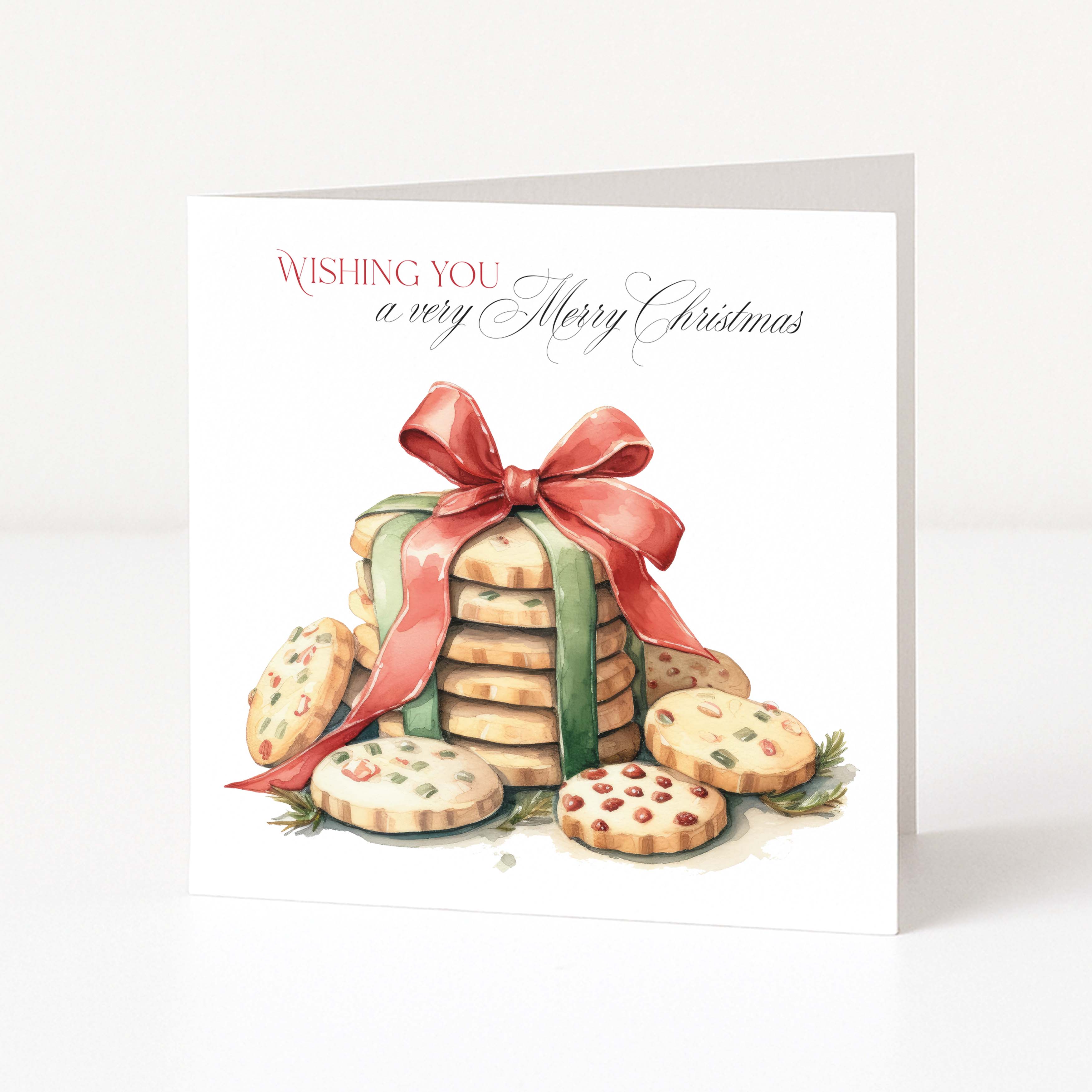 A square Christmas greeting card standing upright on a white surface. The card features an illustration of stacked cookies tied with a red ribbon, with the text 'WISHING YOU a very Merry Christmas' printed at the top.