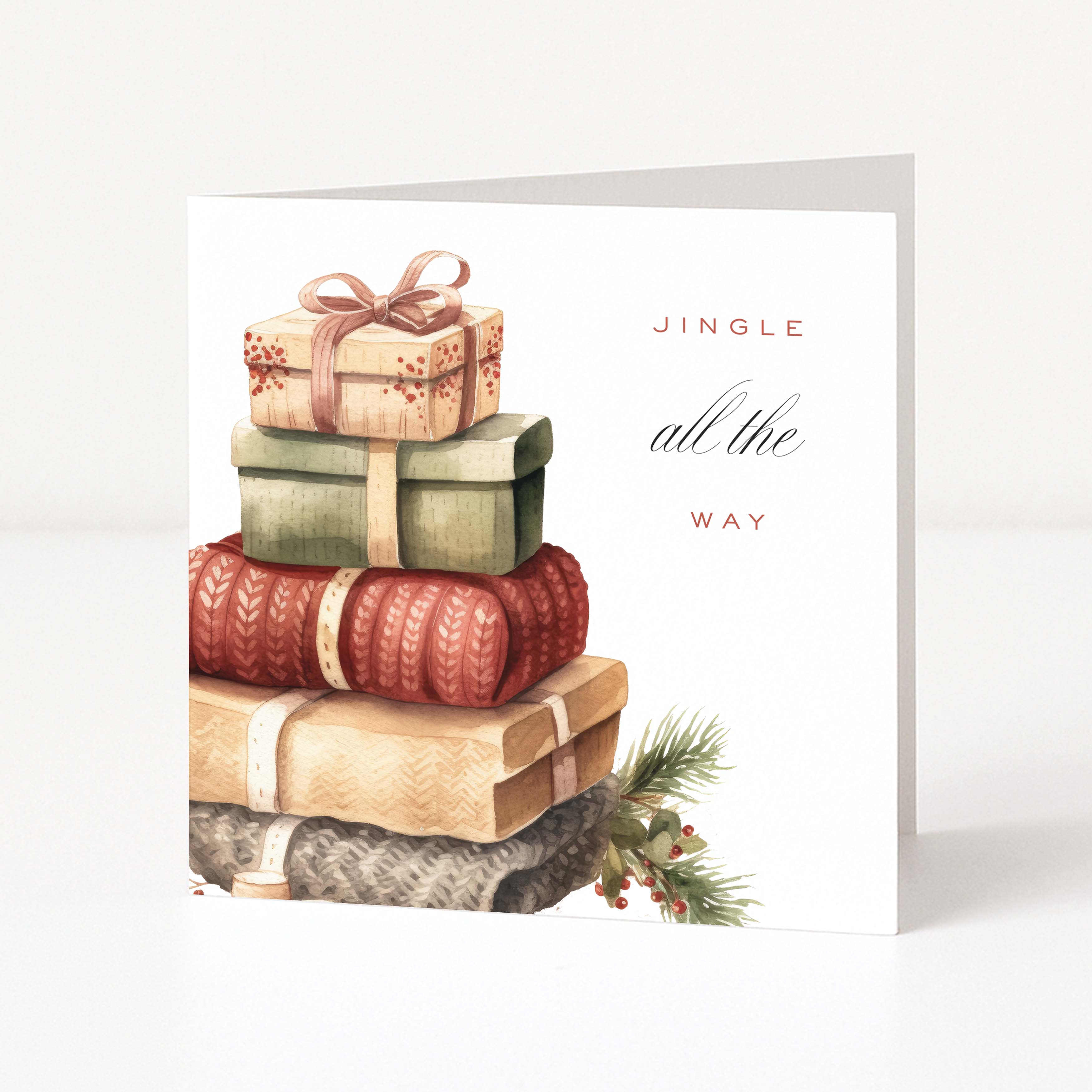 A white Christmas greeting card featuring a watercolour illustration of stacked wrapped gifts in winter colours, with the text 'JINGLE all the WAY' on the right side, photographed against a clean white background.