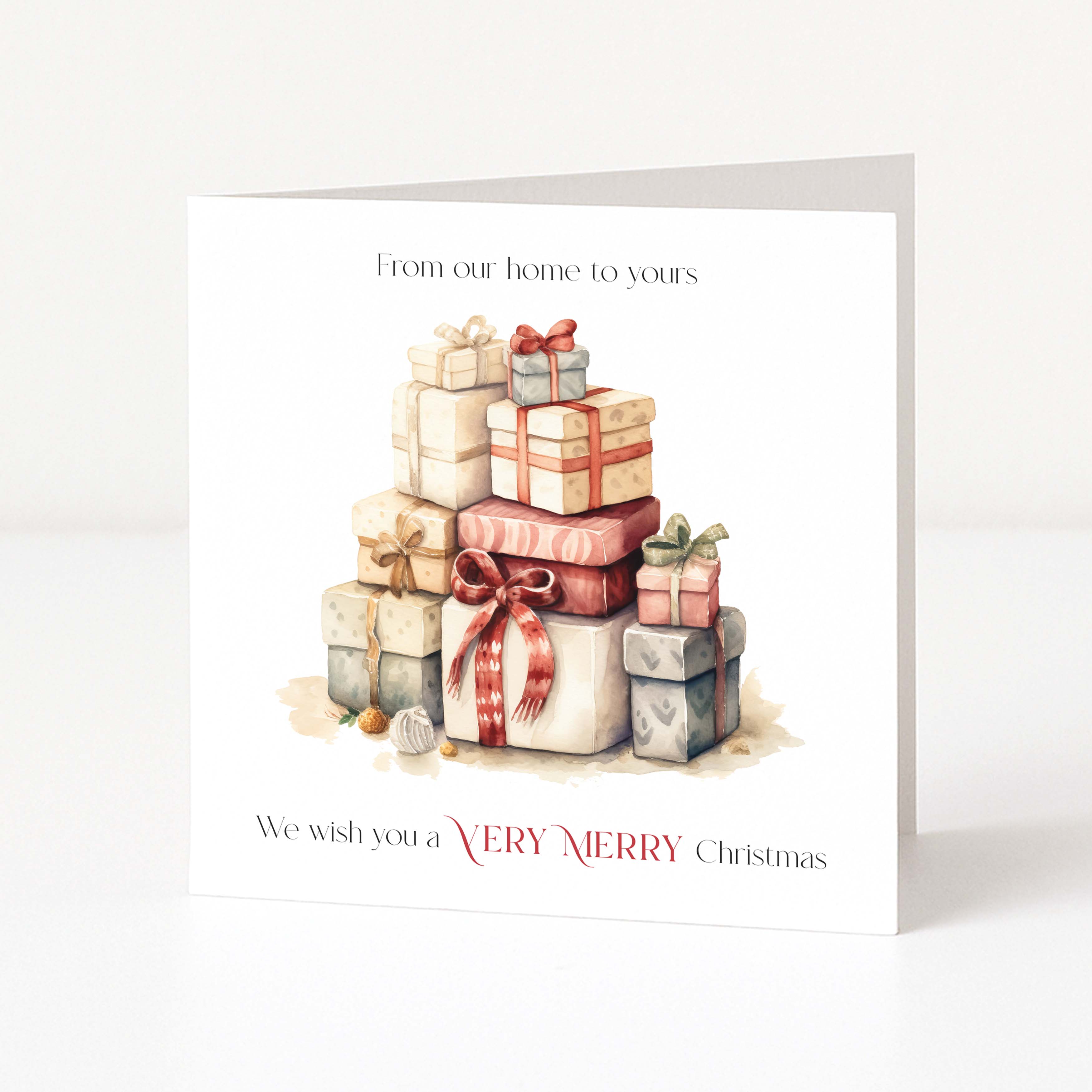 A square Christmas greeting card standing upright on a white surface against a light neutral background. The card features a watercolour illustration of stacked gift boxes with red, pink, beige, and gray wrapping, with the text 'From our home to yours' at the top and 'We wish you a VERY MERRY Christmas' at the bottom.