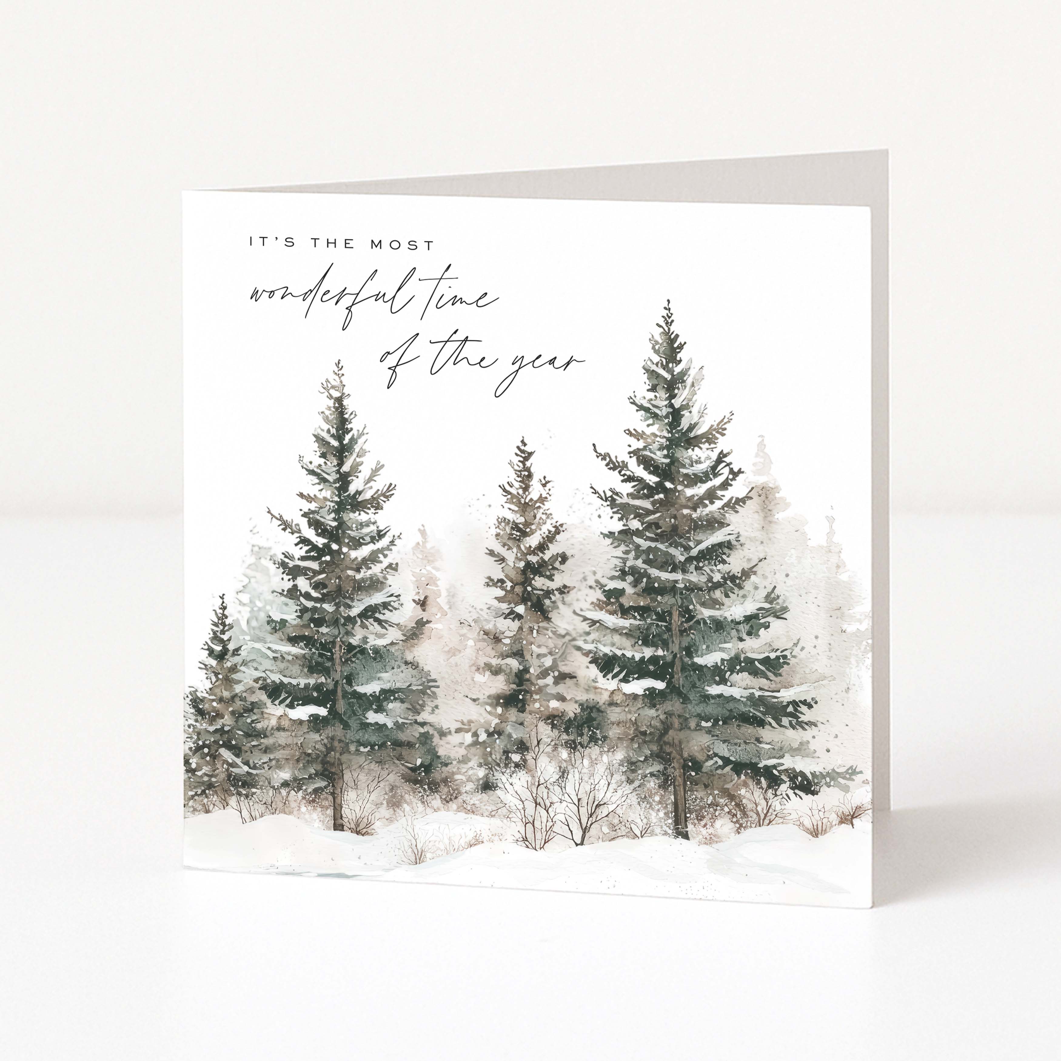 A square Christmas greeting card with a winter forest illustration, featuring snow-covered evergreen trees and the text 'IT'S THE MOST wonderful time of the year' on a white background.
