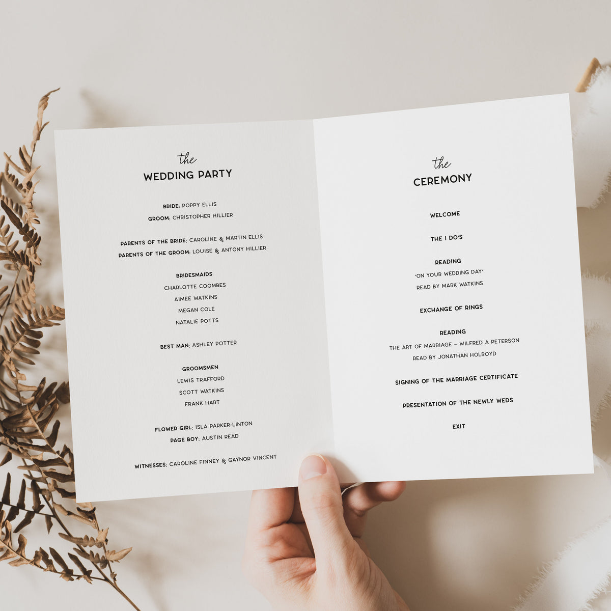 An open wedding program booklet displayed on a person's hands against a warm beige background with dried floral accents. The booklet contains printed event details in black text.